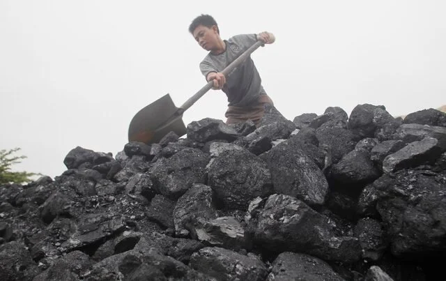 Child using a shovel to move black coal or rocks outdoors.