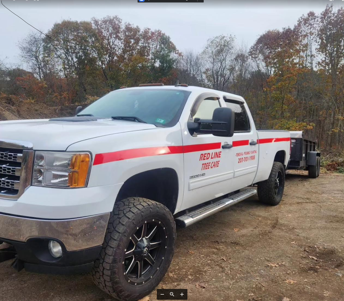 White pickup truck with red stripe and 'Red Line Tree Care' written on the side, parked on a dirt path with autumn trees in the background. Red Line Tree Care.
