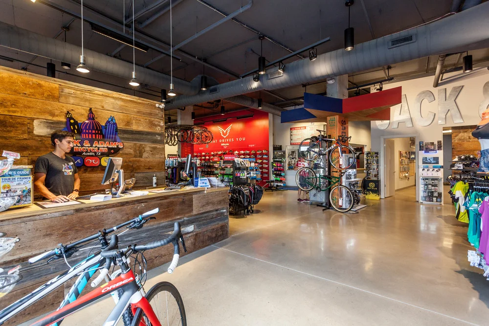 Jack and Adams retail buildout by Forsite Studio — bike shop interior with wood front counter, staff at register, and bicycles on display — Austin, TX