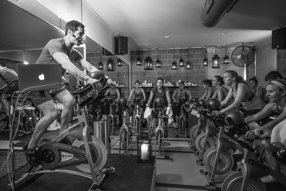 DEFINE Austin fitness studio by Forsite Studio — instructor-led spin class with participants on stationary bikes in dim lighting — Austin, TX