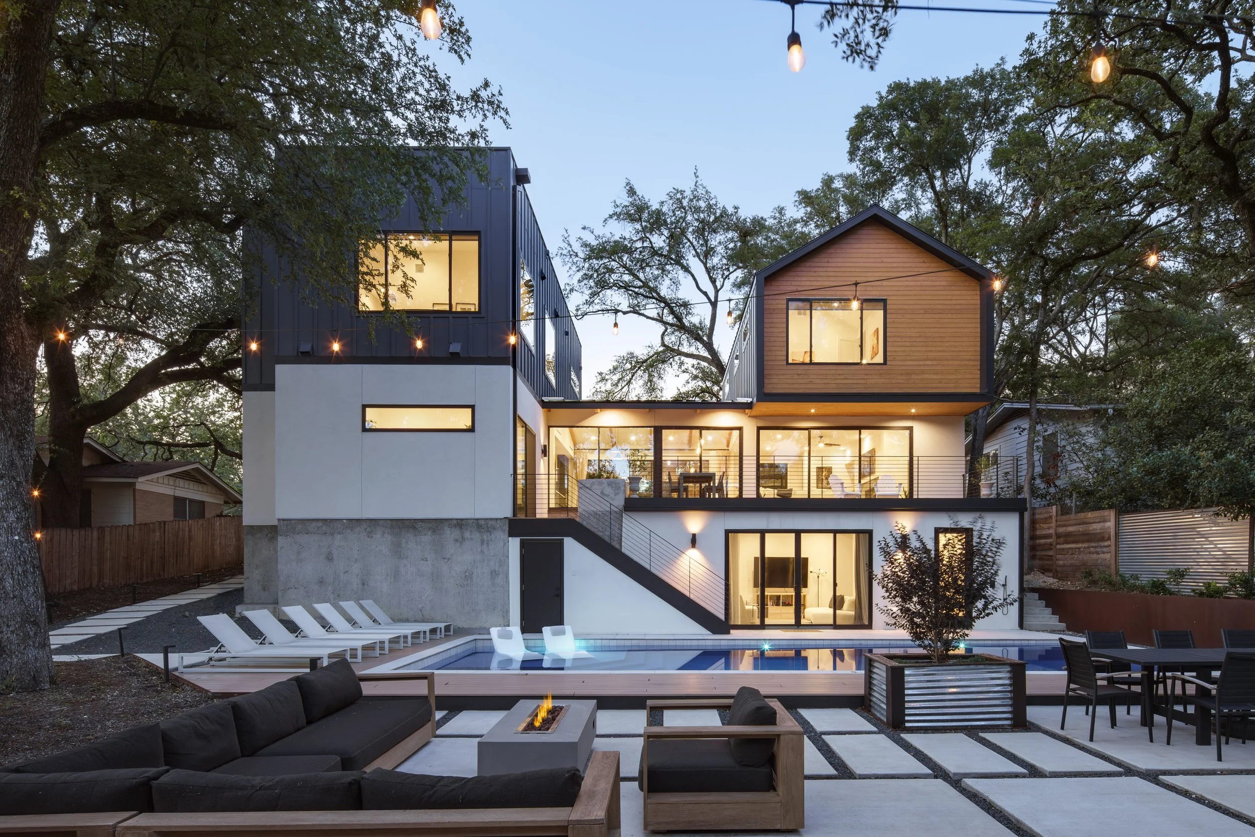 Mariposa Residence by Forsite Studio — rear elevation at
dusk from the patio, firepit and dining terrace beside a lit pool under
 string lights — Austin, TX