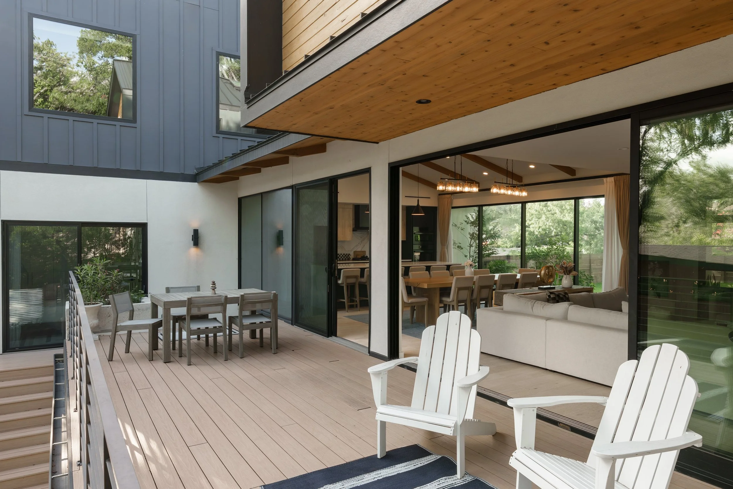 Mariposa Residence by Forsite Studio — covered upper
deck with dining table and Adirondack chairs opening into the living
room — Austin, TX