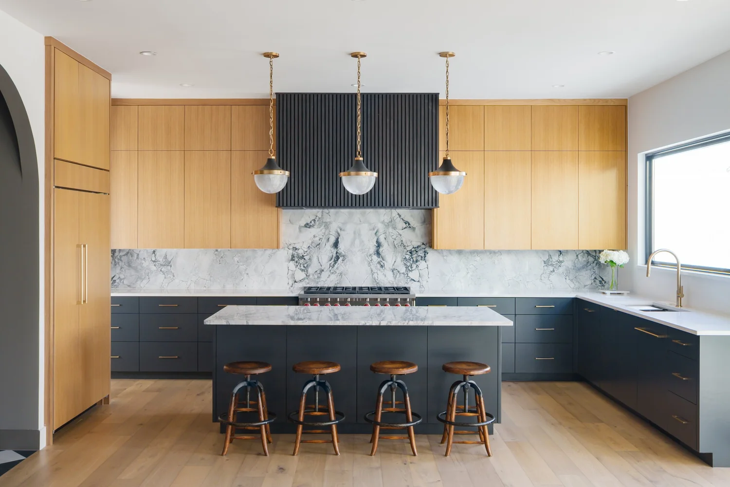 Terrace residence by Forsite Studio — kitchen with marble island, black and wood cabinetry, and three pendant lights — Austin, TX