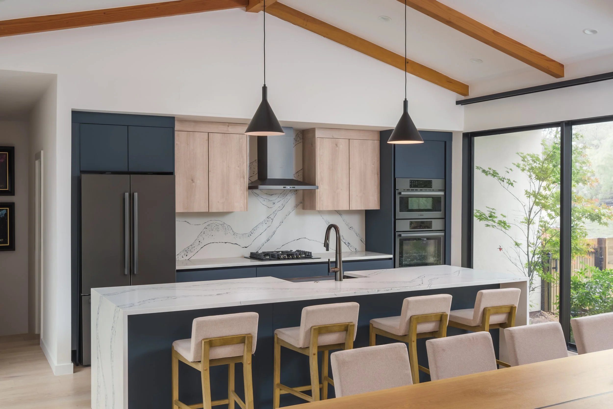 Mariposa Residence by Forsite Studio — kitchen with deep
blue cabinetry, white oak uppers, and a veined quartz island under
exposed beams — Austin, TX