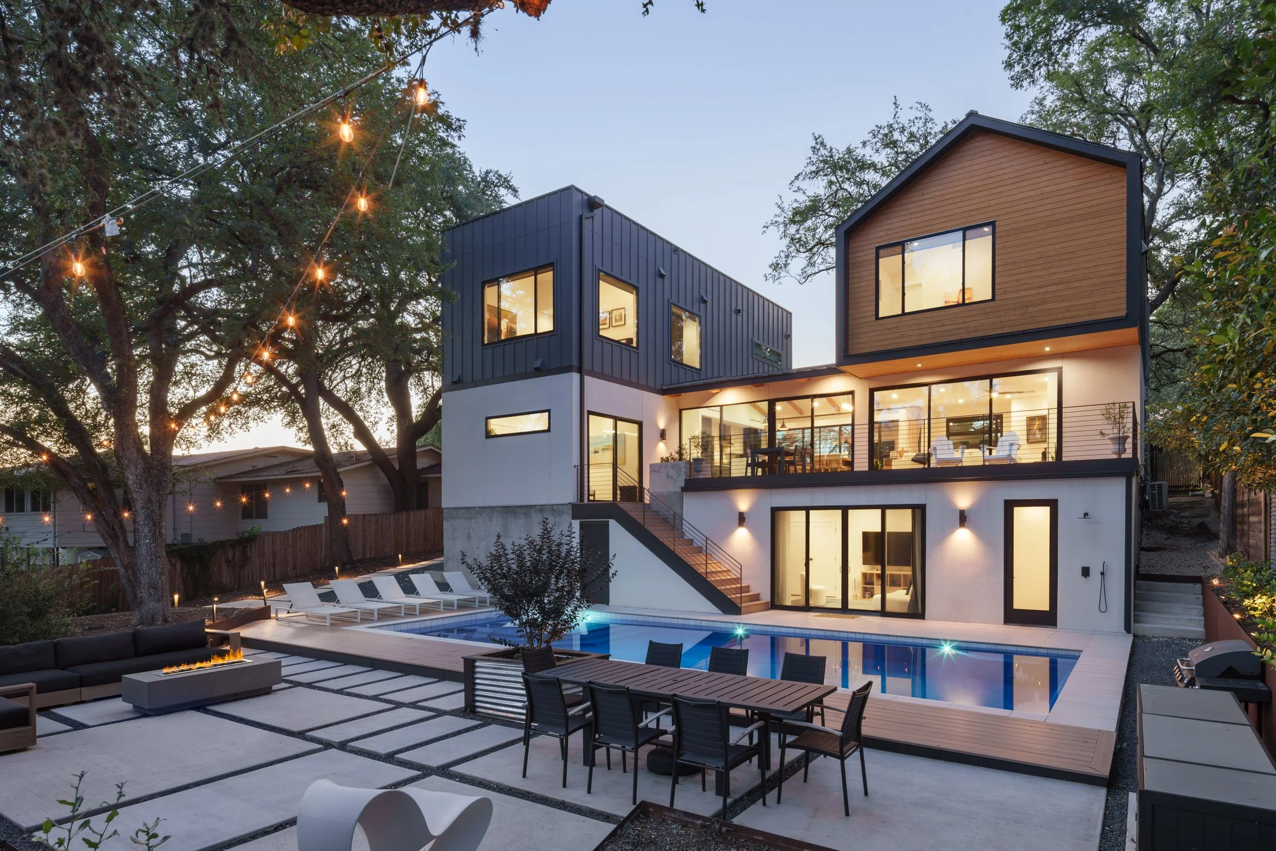 Mariposa Residence by Forsite Studio — rear elevation at
dusk from the patio, firepit and dining terrace beside a lit pool under
 string lights — Austin, TX