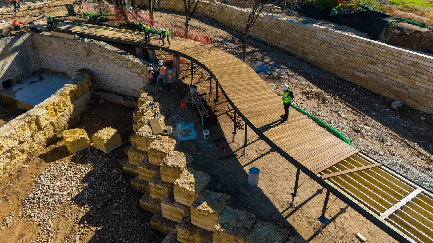 Waller Creek decking & cladding by Forsite Studio — construction workers installing curved wood walkway on metal framework — Austin, TX