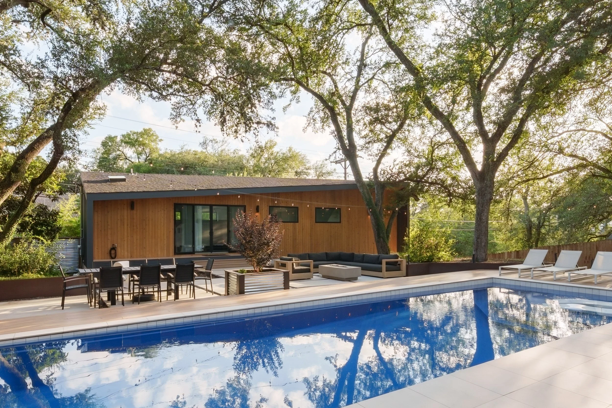 Mariposa Residence by Forsite Studio — pool in late
afternoon light facing the cedar-clad pool house beneath live oaks —
Austin, TX