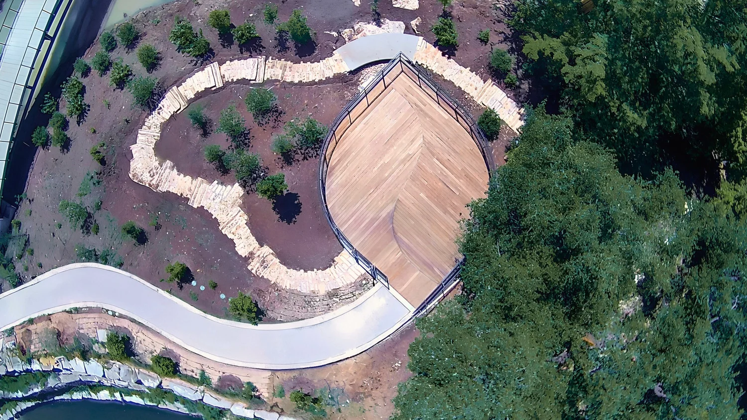 Leaf decking & cladding by Forsite Studio — aerial view of landscaped park with winding white path, young trees, and wood deck area — Austin, TX