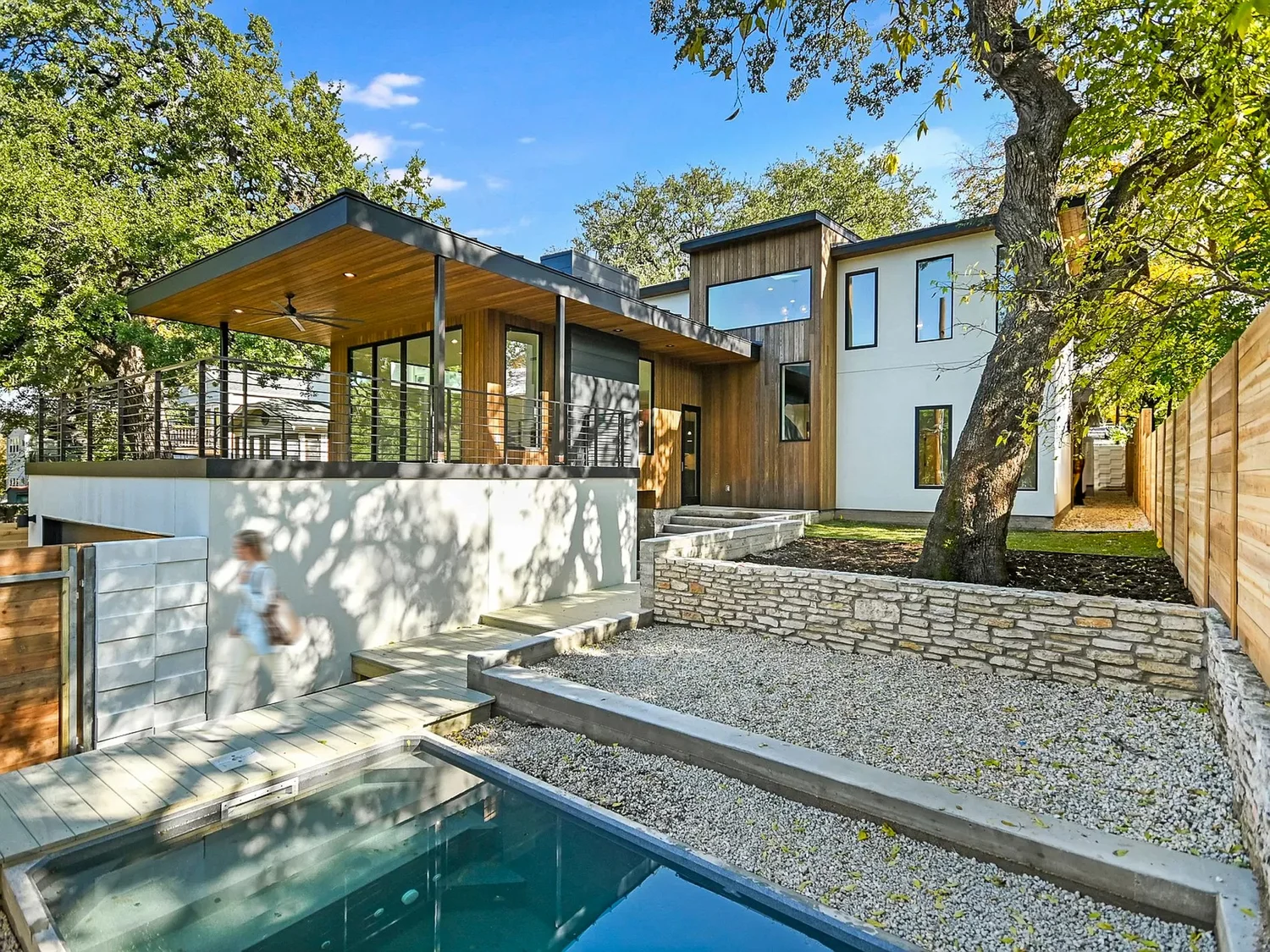 Alameda residence by Forsite Studio — wood and white exterior with large window and spacious patio surrounded by trees — Austin, TX