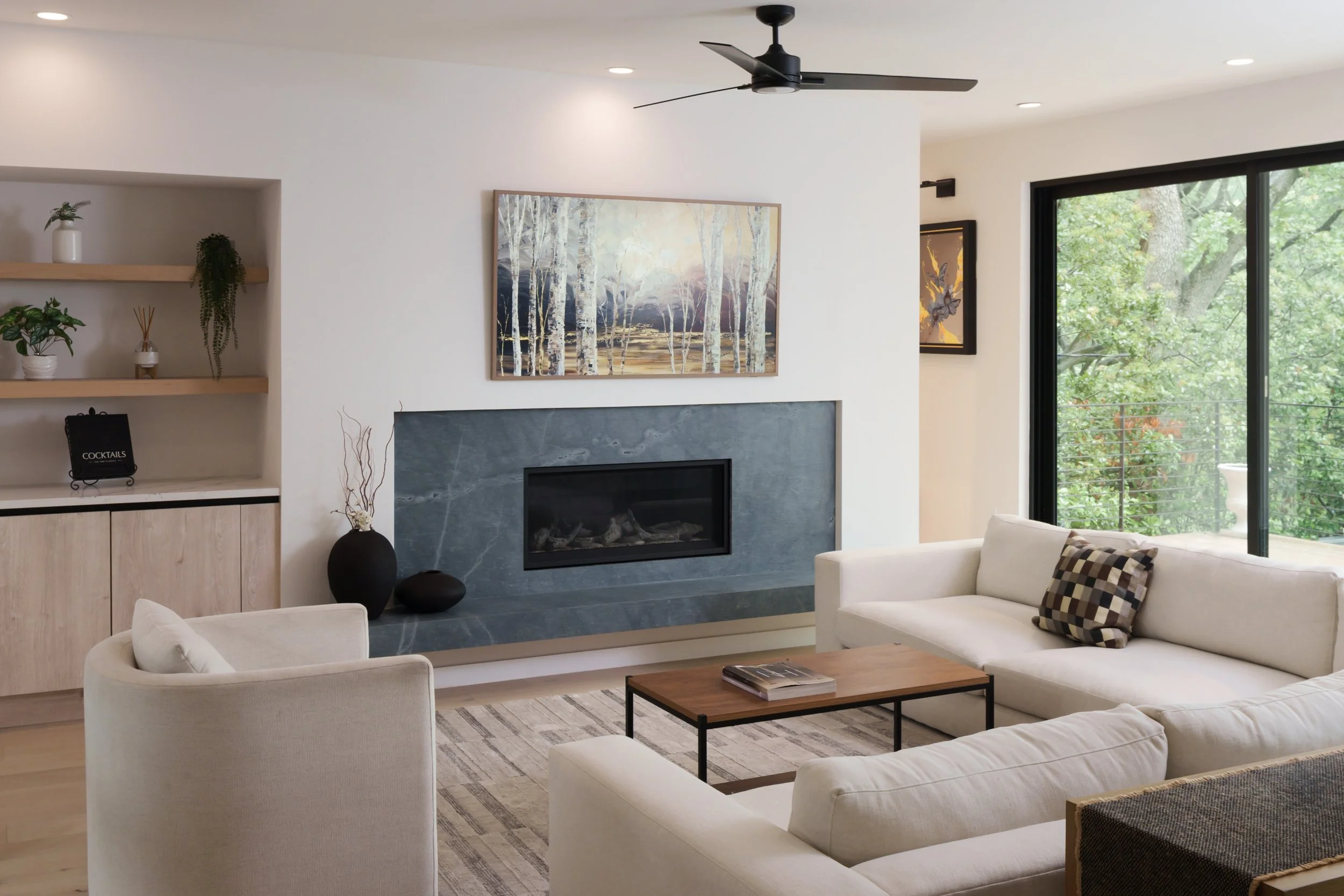 Mariposa Residence by Forsite Studio — living room with
a full-width dark stone fireplace, floating hearth, oak shelving, and
glass to the treetops — Austin, TX