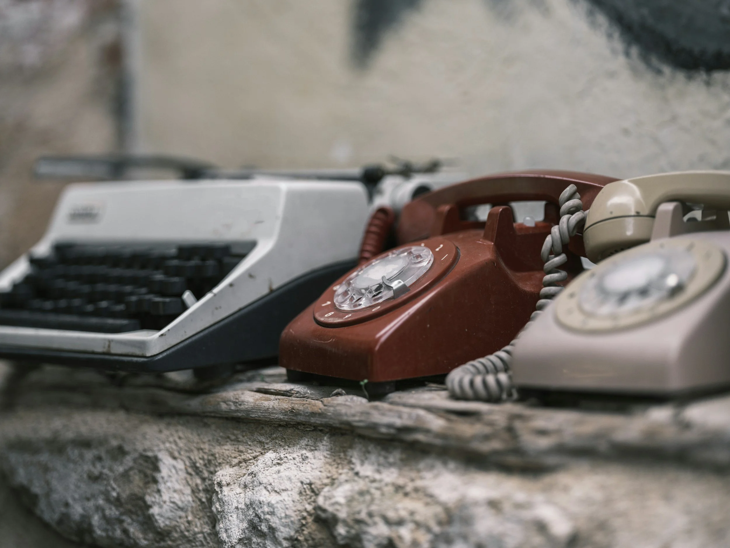Three vintage rotary phones in brown, beige, and black colors placed on a rustic wooden surface.