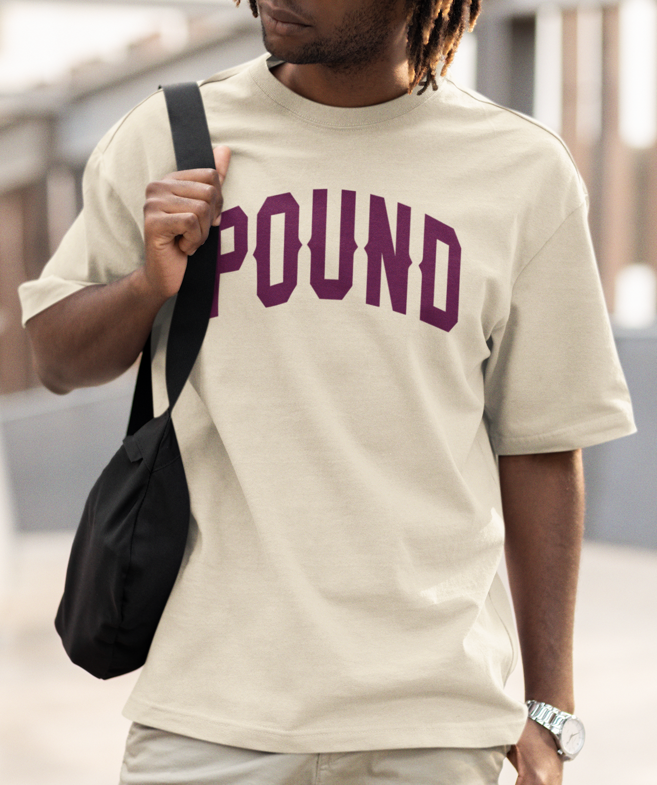Man showing the back of her shirt, oversized tee with short dark hair, wearing a powder blue T-shirt with the word 'pound' printed in Navy Blue, Assembled in North Hollywood, California.