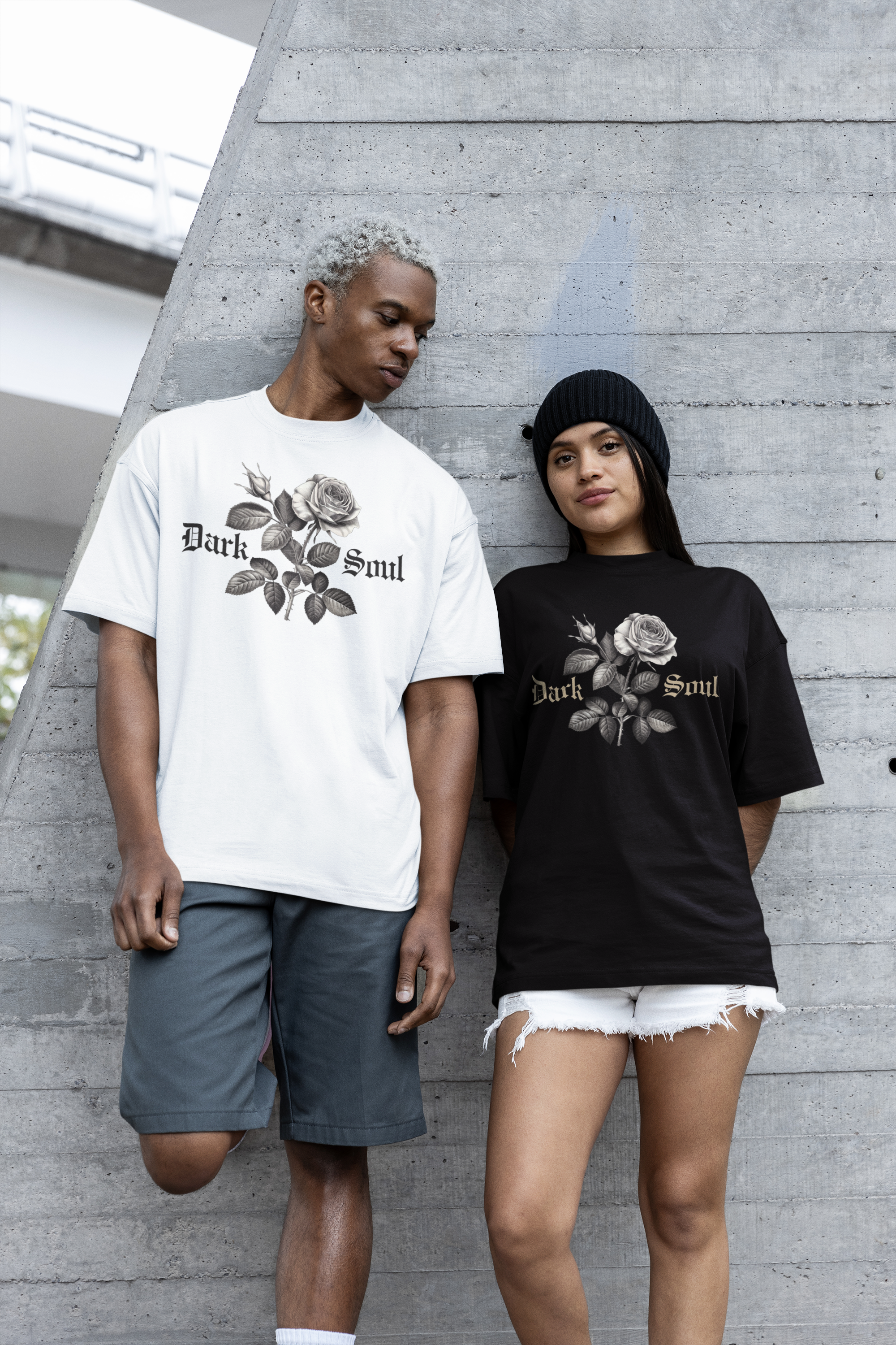A young man with gray hair and a young woman with a beanie standing against a concrete wall, both wearing T-shirts with a rose design and the words 'Dark Soul'.