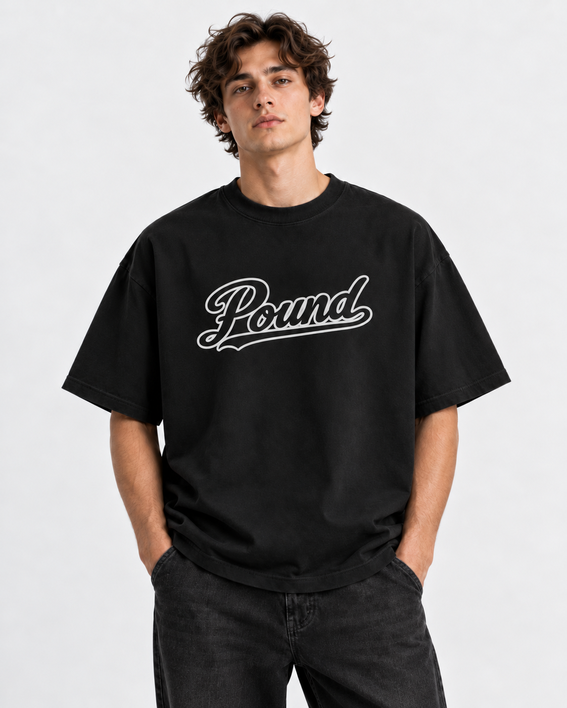 Young man with curly brown hair wearing a black T-shirt with the word 'Pound' written across it in cursive font, standing against a plain light gray background.
