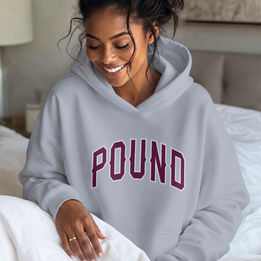 Soft light gray pullover hoodie with an arched maroon-and-white “POUND” varsity print. Relaxed, cozy fit.