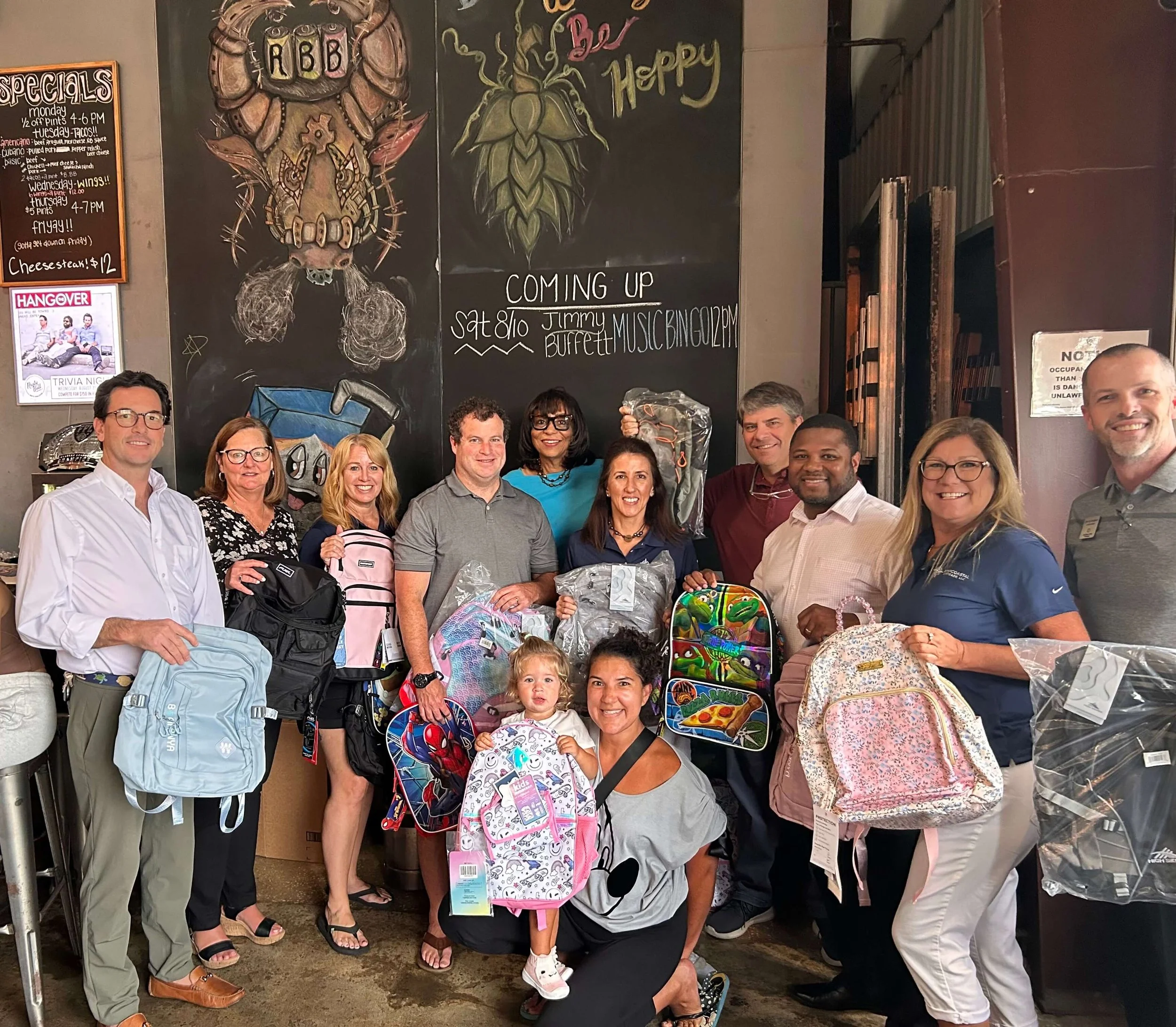 Group of people holding backpacks inside a shop, chalkboard art in background.
