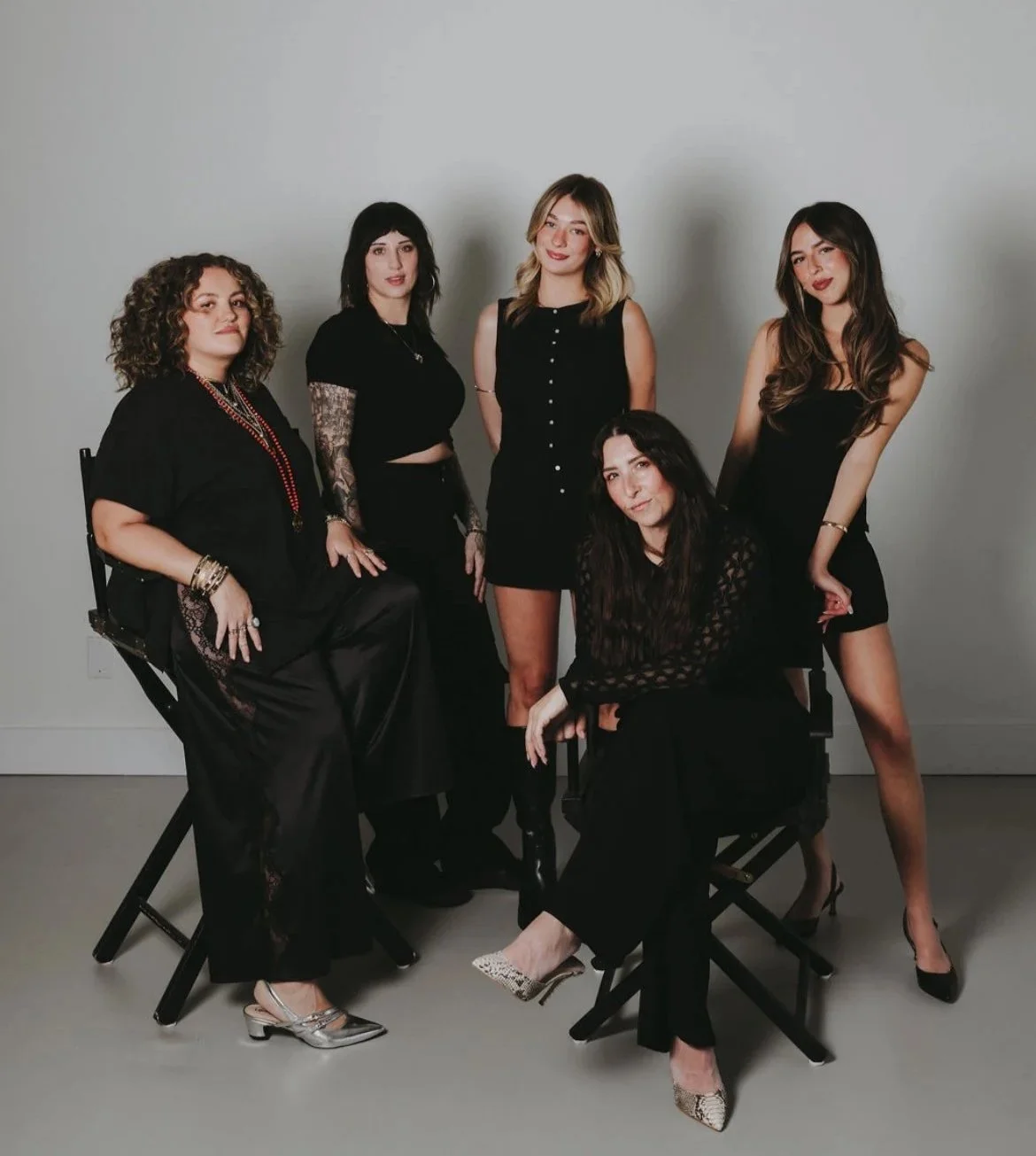 Salon team photo of five Vero Beach hairstylists  in black outfits posing against a plain background, some seated and some standing.