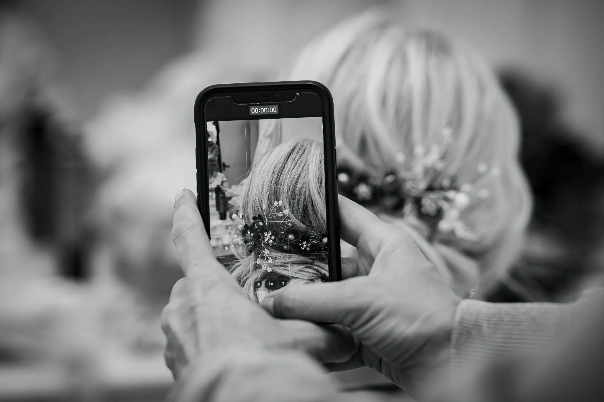 Person taking a photograph of a woman wearing a floral headpiece with a smartphone.