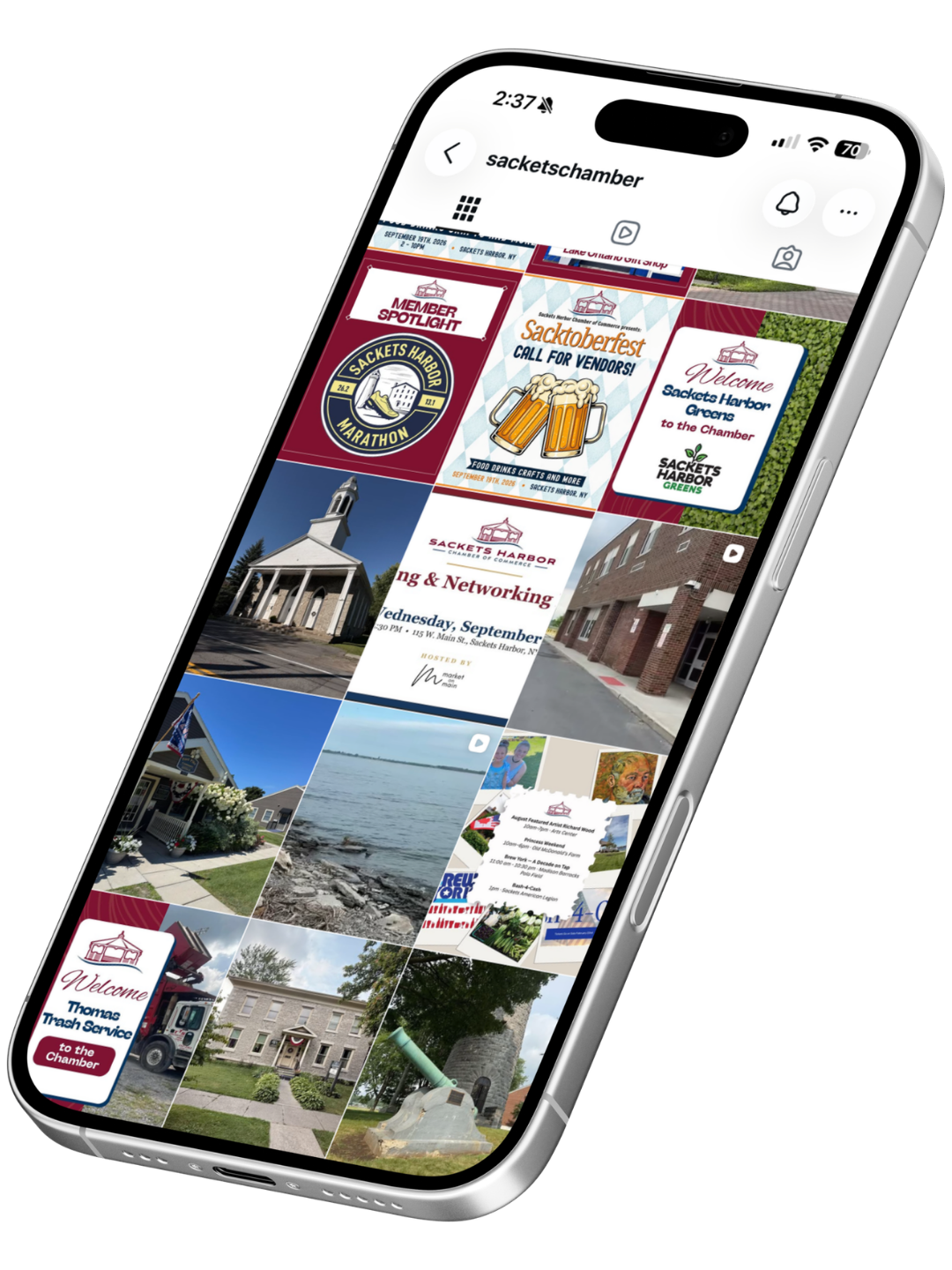 A smartphone displaying a social media profile of Sackets Chamber featuring various colorful event flyers, community photos, and welcome signs in a grid layout from Sackets Harbor Chamber's Instagram