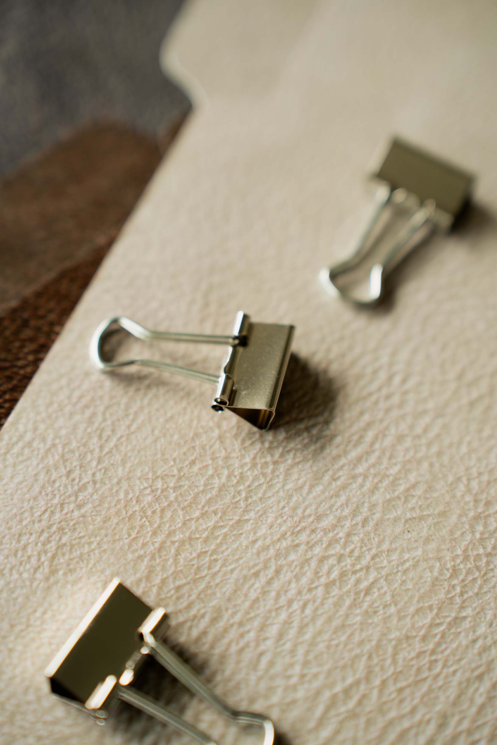 Close-up of metal binder clips on a textured beige surface.