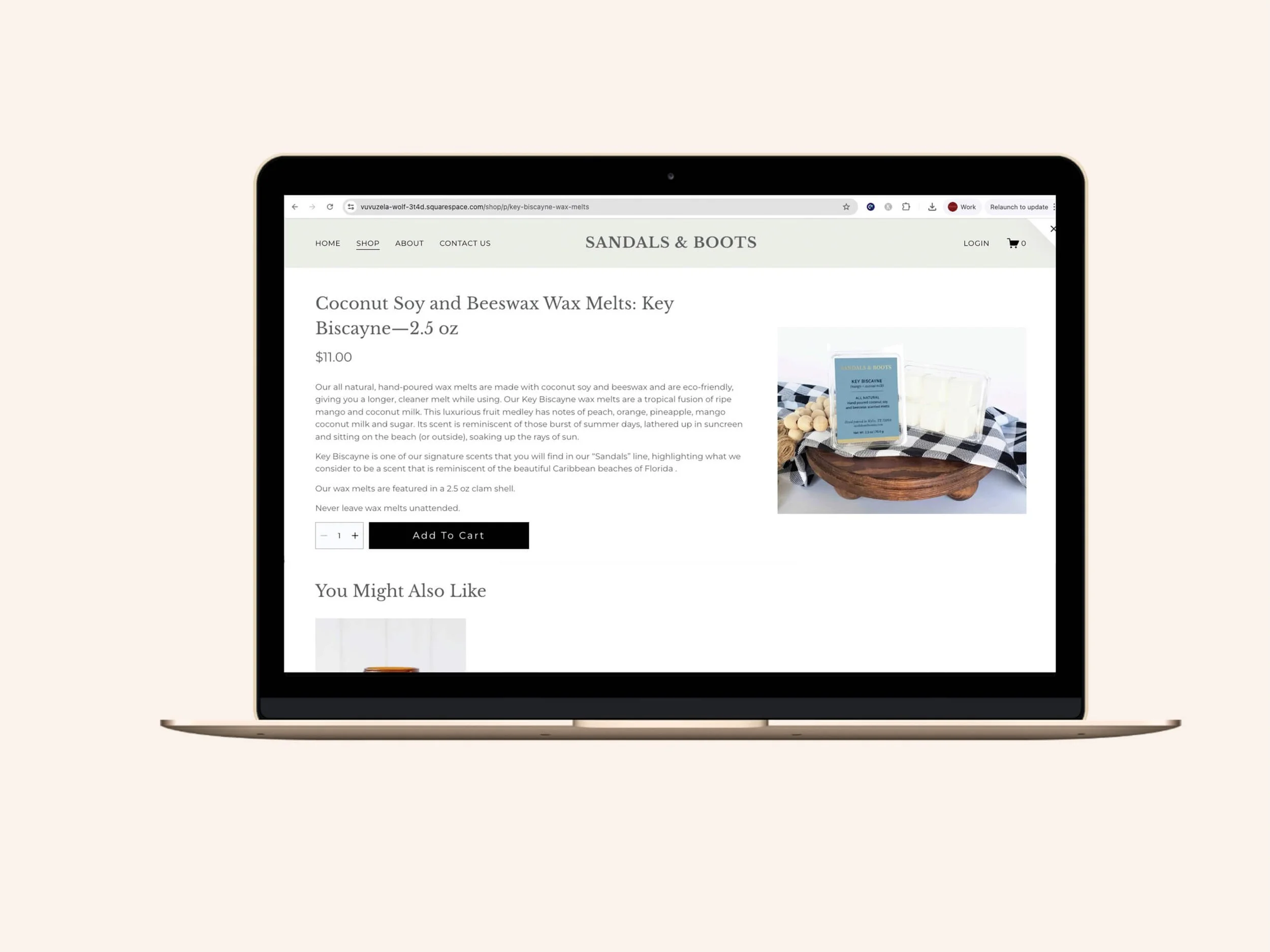 Screenshot of the Sandals & Boots product detail page displayed on a gold MacBook laptop, showing the listing for a 2.5 oz. Key Biscayne coconut soy and beeswax wax melt with product description, $11.00 pricing, an Add To Cart button, and a styled pr