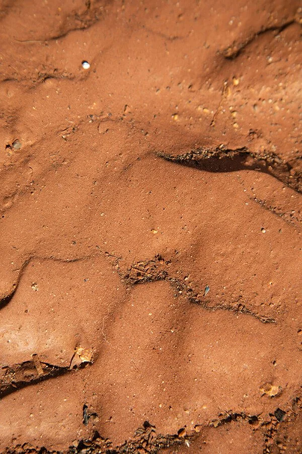 Close-up of red clay soil with small rocks and cracks.
