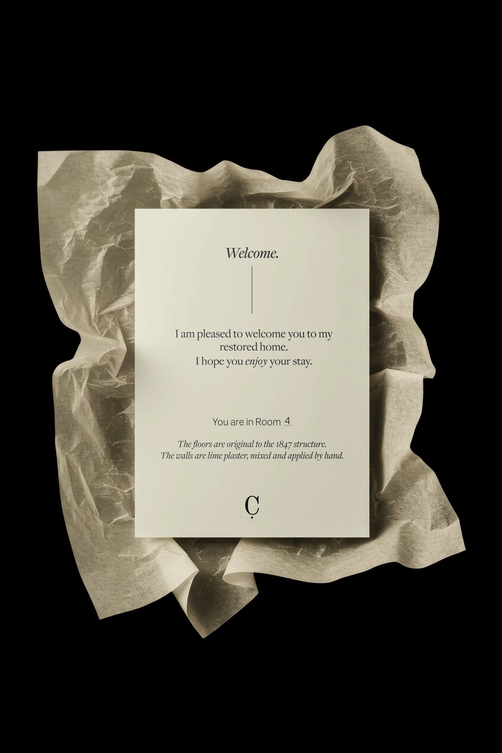 A welcome note on a piece of paper with a vintage background of crumpled paper and dark background, stating: 'Welcome. I am pleased to welcome you to my restored home. I hope you enjoy your stay. You are in Room 4. The floors are original to the 1847 structure. The walls are lime plaster, mixed and applied by hand.'