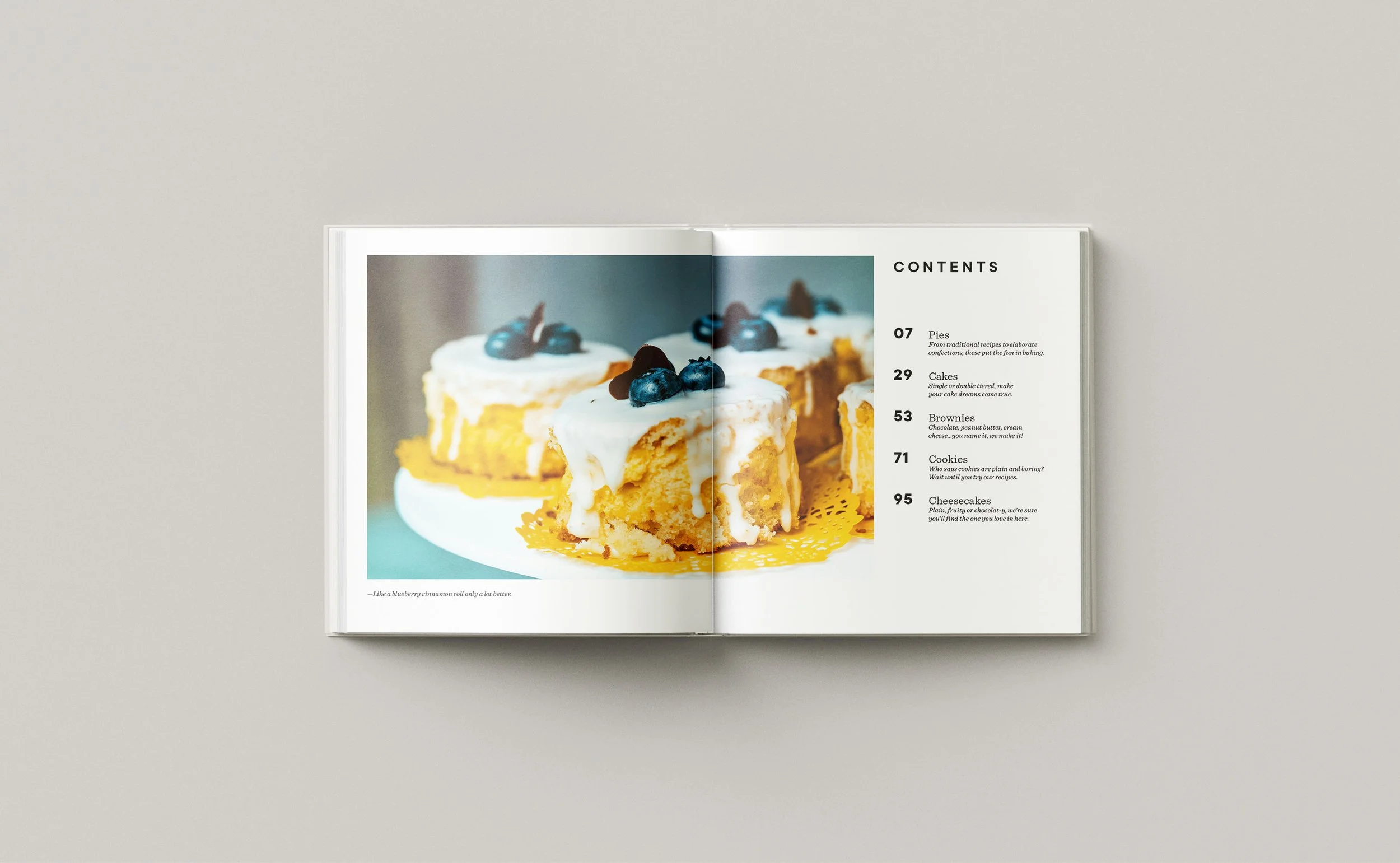 Cookbook table of contents spread. Left page features a full-bleed food photograph of frosted blueberry cake slices with a caption below. Right page lists five chapters with page numbers and brief descriptions: Pies (07), Cakes (29), Brownies (53), C