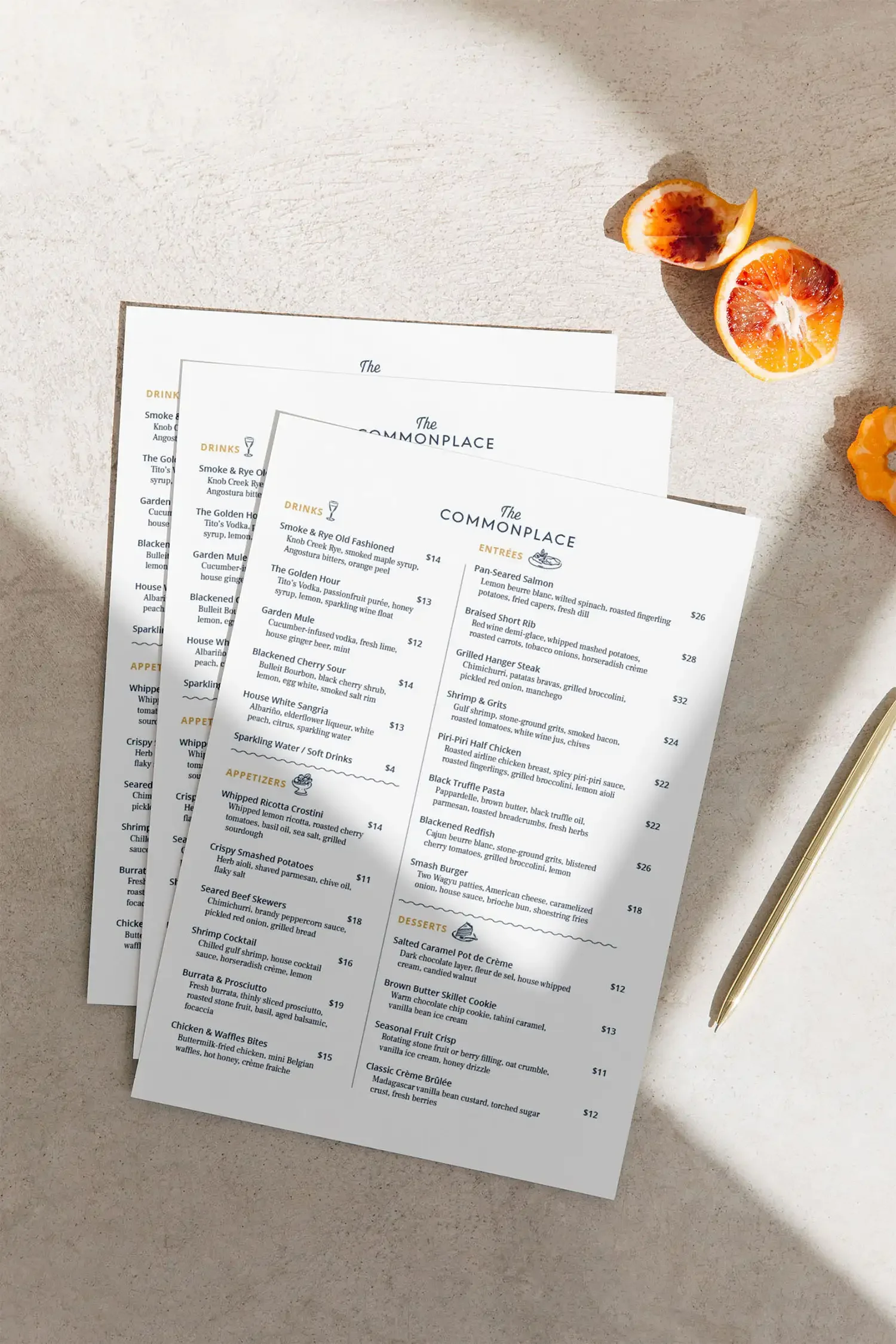 A menu placed on a flat surface with a golden pen beside it, along with sliced citrus fruits in the background.