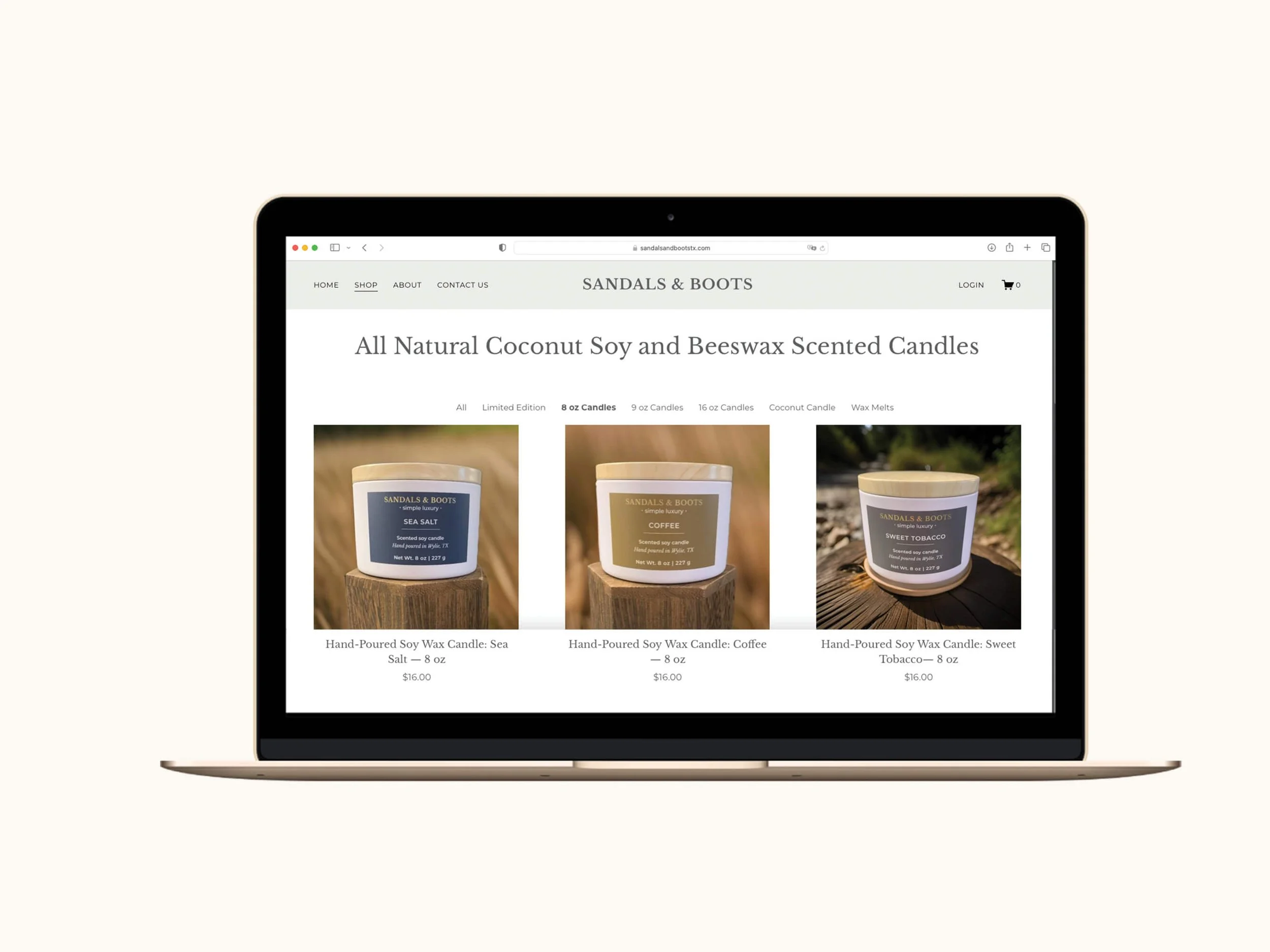 Screenshot of the Sandals & Boots shop page displayed on a gold MacBook laptop, showing the 8 oz. candle category filtered view with three hand-poured soy wax candles — Sea Salt, Coffee, and Sweet Tobacco — each priced at $16.00.
