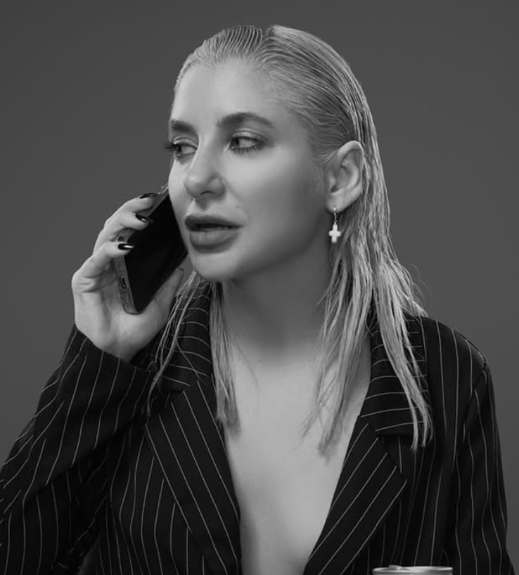 A woman with wet hair, wearing a pinstripe blazer and cross earrings, is speaking on a mobile phone.