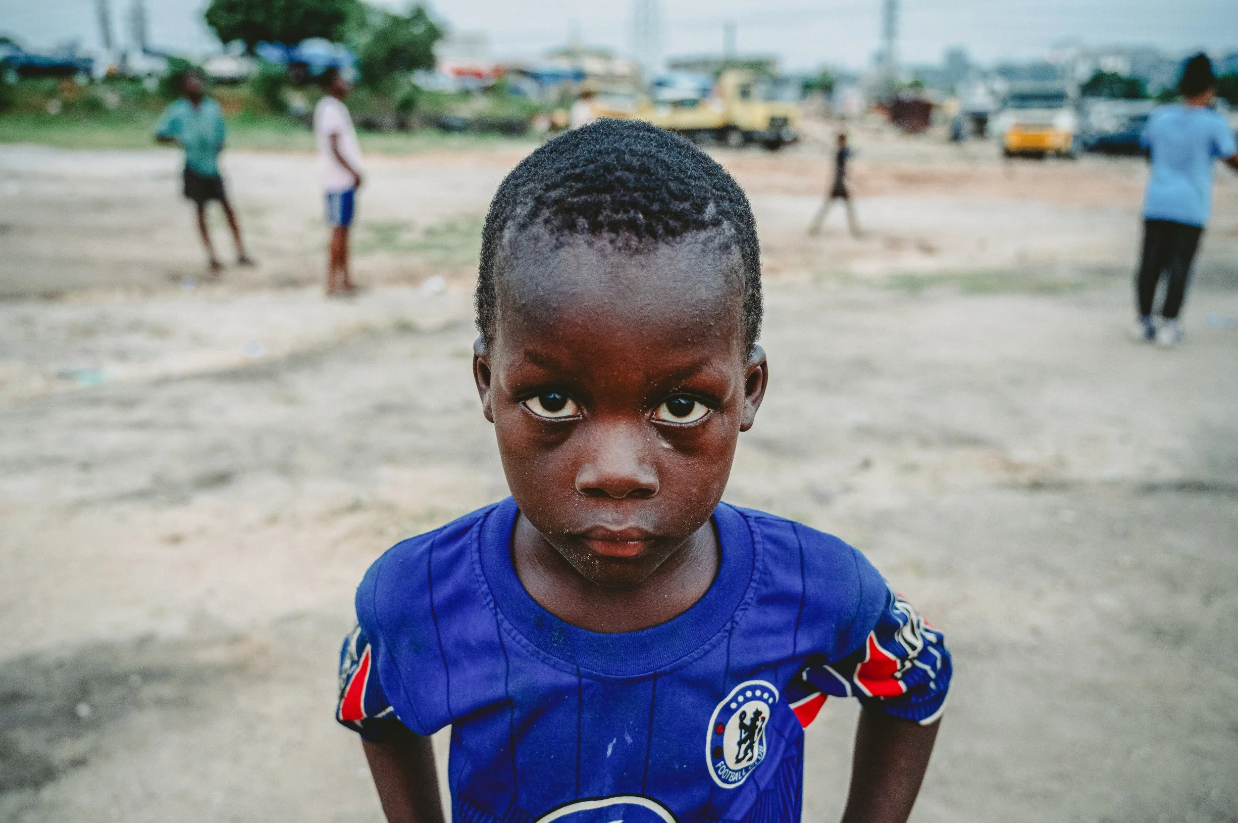 Umbasso plays football in the street with friends while his mother works in a food stall up the road. 