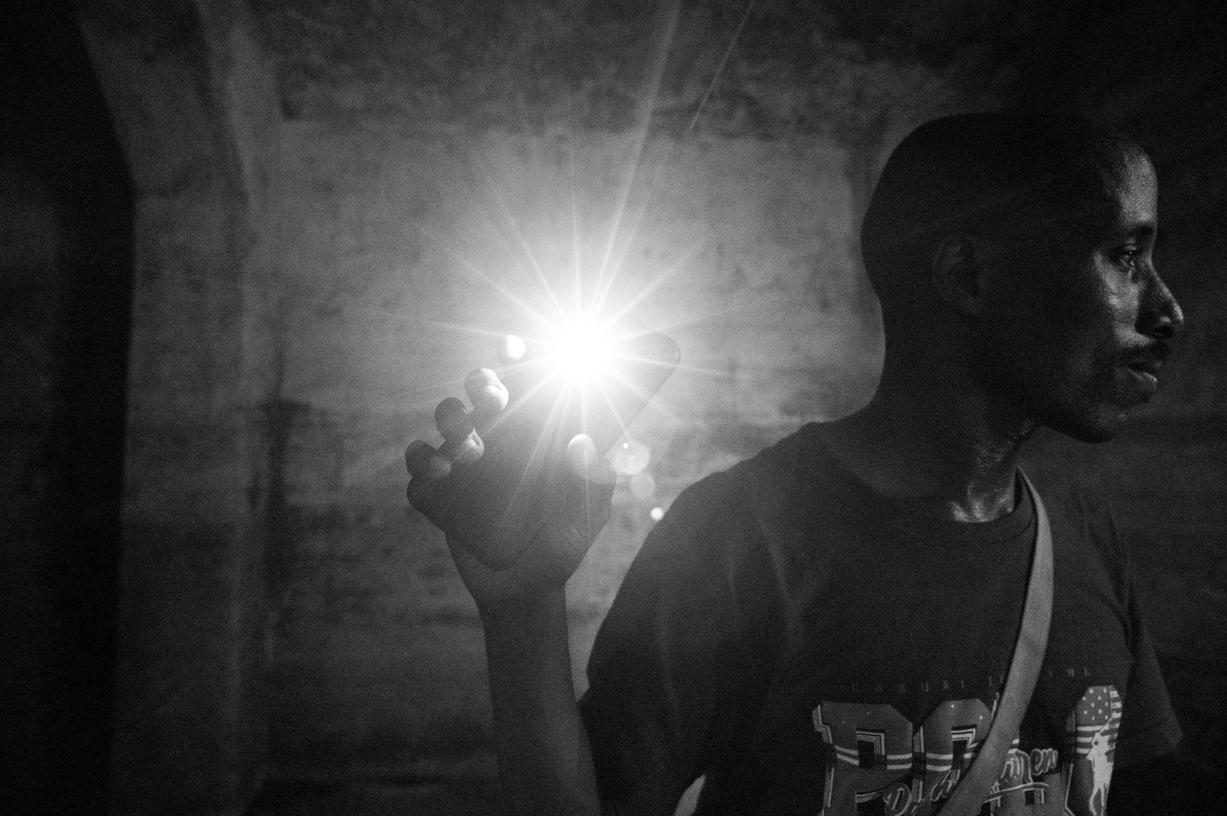 A man uses his phone flashlight to see the walls of an abandoned slave holding dungeon.