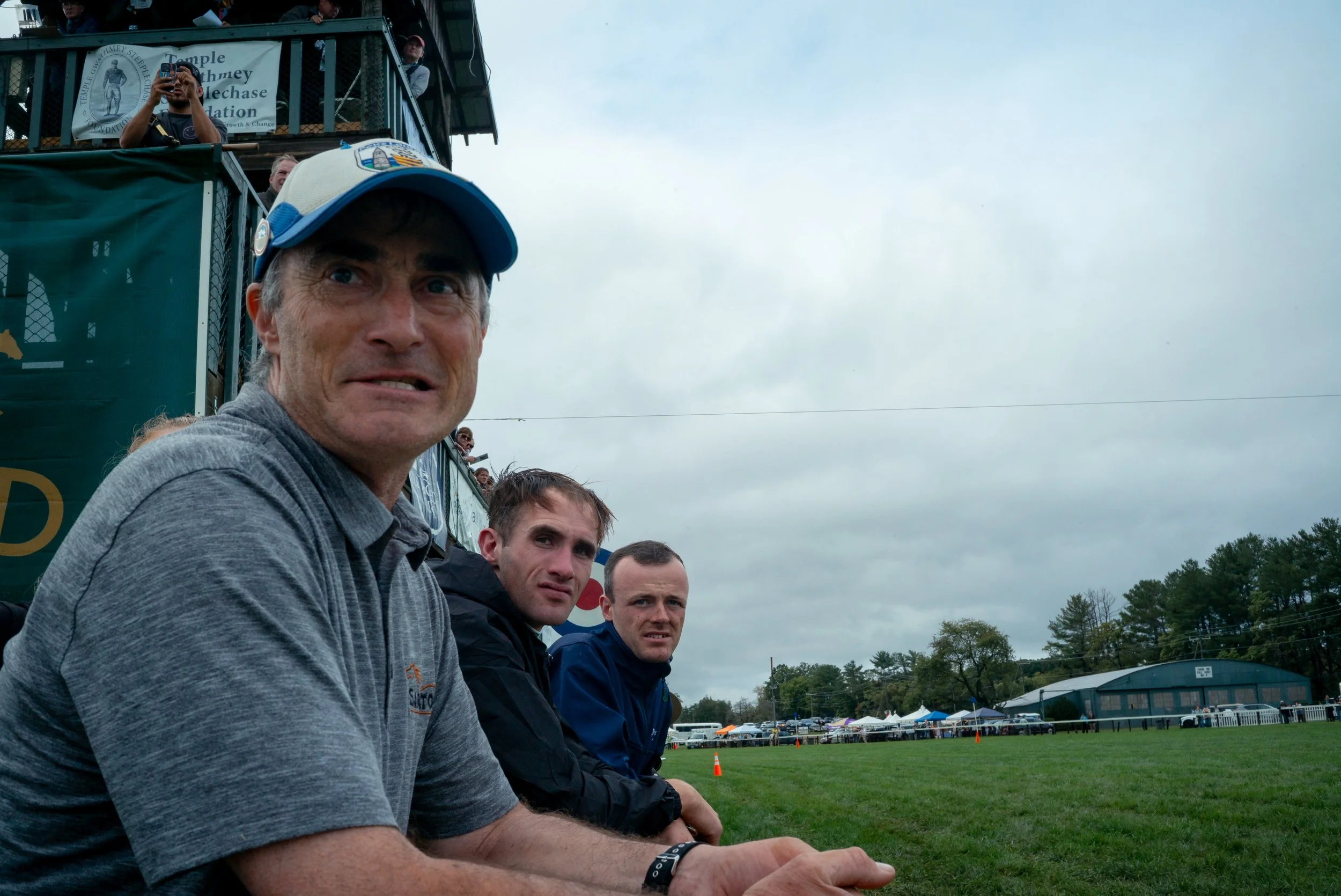 Two jockeys and a trainer watch as riders approach the finish of a race.