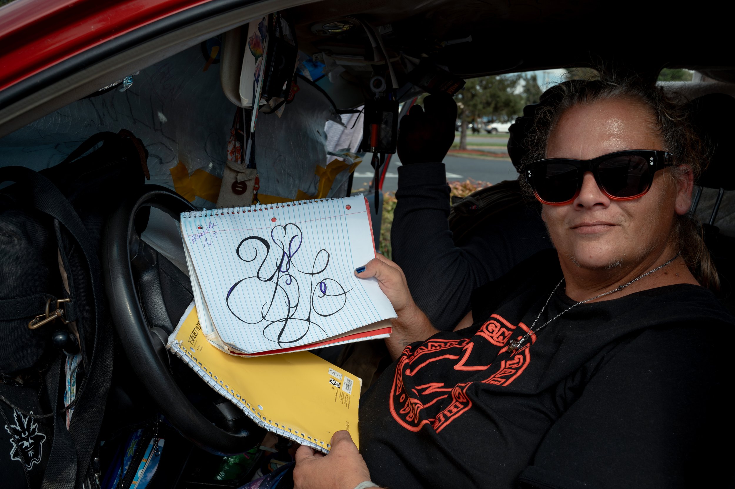 Heather writes “YOLO” in calligraphy for fun while sitting inside her car, where she and her boyfriend Damon lived for nearly three years before the vehicle was taken in January. The couple had moved into the car after Heather could no longer afford 