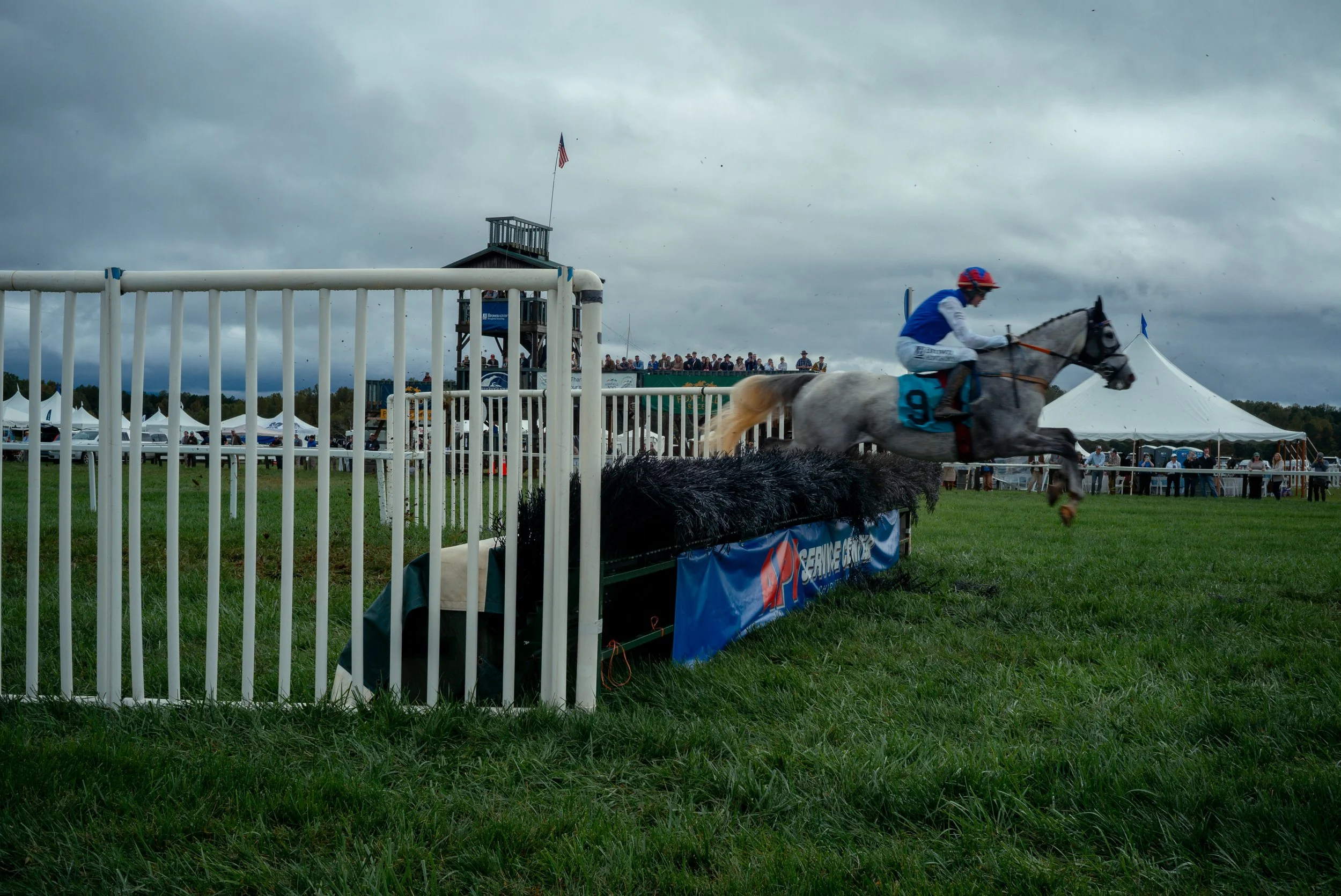 Jockeys guide their horses over a hurdle, kicking dirt and mud into the air during the Foxfield Fall Races on Sunday, Oct. 4, 2026, in Albemarle County, Va.