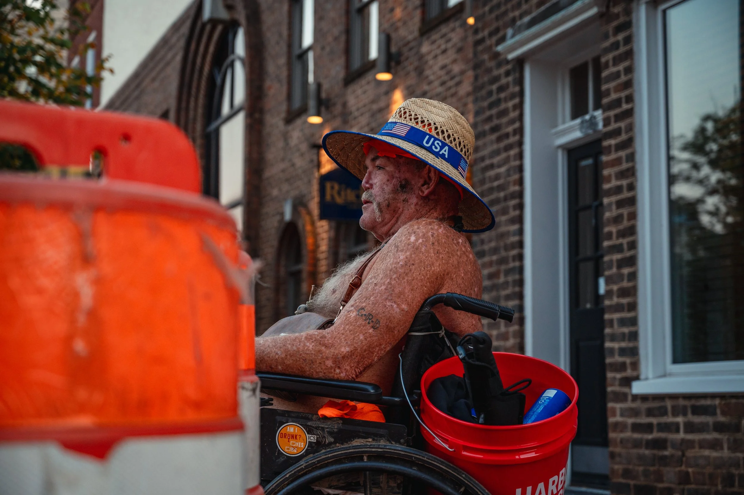 Buck, a double-leg amputee, sits in his wheelchair while wearing his favorite “USA” sunhat in downtown Harrisonburg. After losing both legs to diabetes, Buck moved to Harrisonburg in search of a more comfortable living situation. He spends his days o
