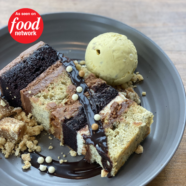 Slices of cake with chocolate drizzle, a scoop of vanilla ice cream, and cookie crumbs on a gray plate.