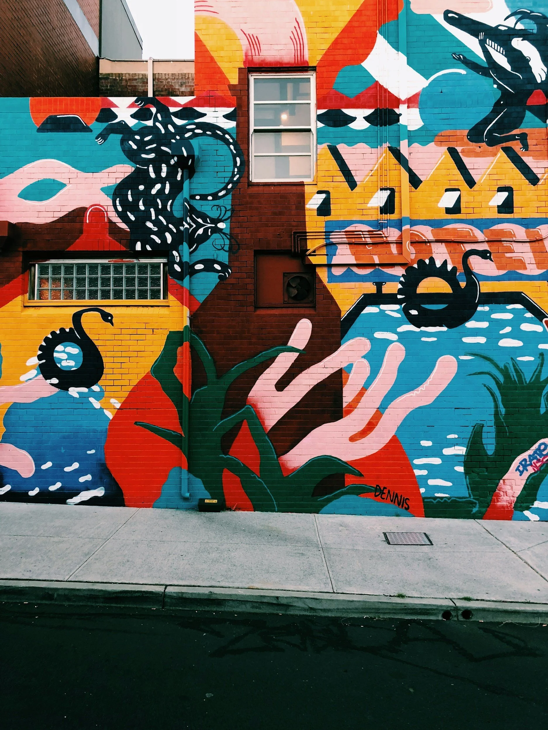 Colorful mural on a brick wall featuring abstract shapes and images of swans and a snake, with the signatures 'DENNIS' and 'ZARD'.