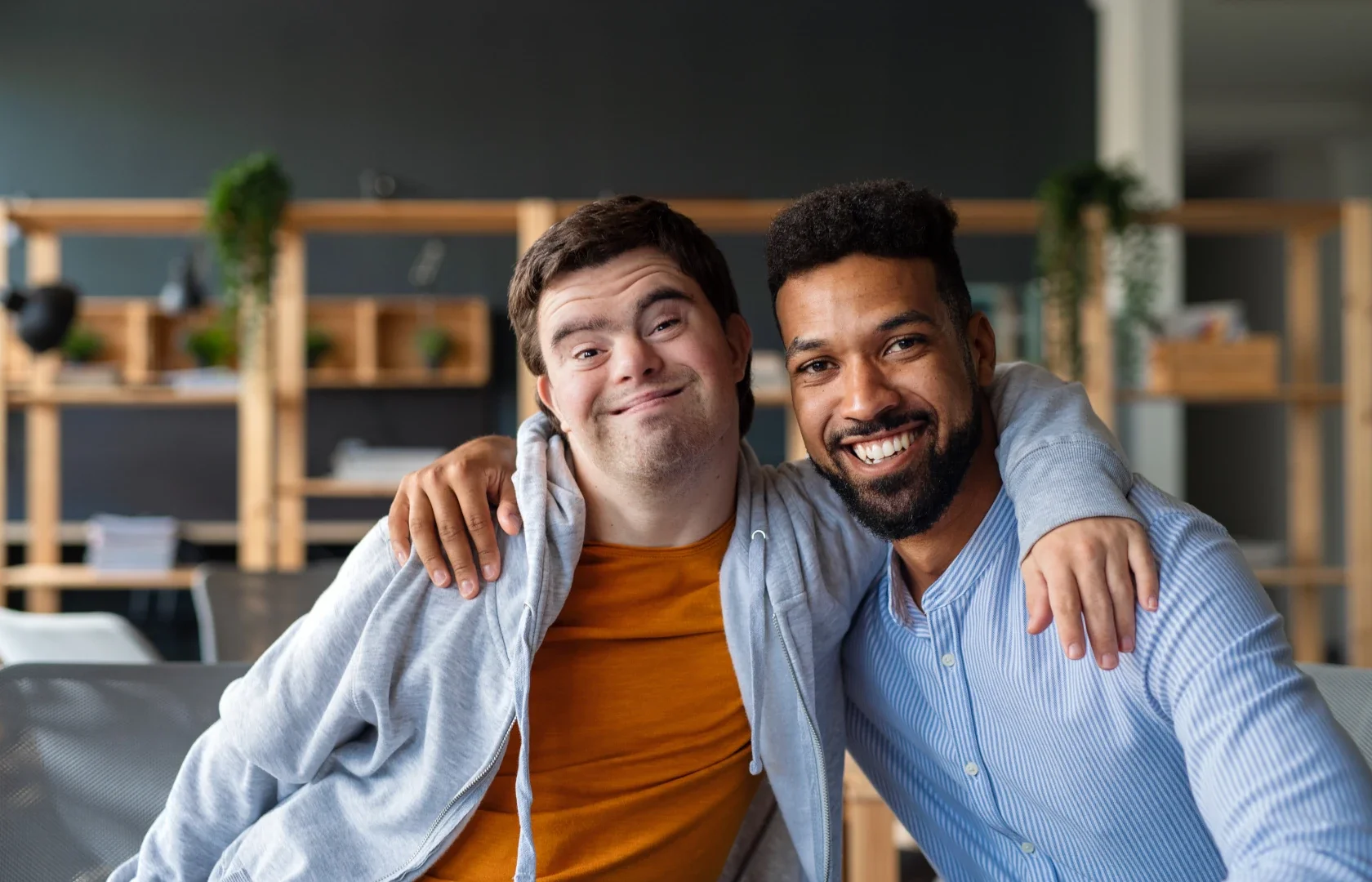 Two smiling men with one arm around each other's shoulders, posing together indoors.