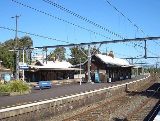 A small train station with a covered platform and train tracks, under a clear blue sky.