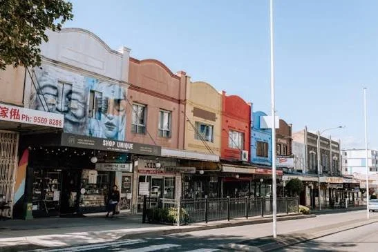 Colorful building facades with shops on the street, including signage for a unique shop and a beauty salon, under a clear blue sky.