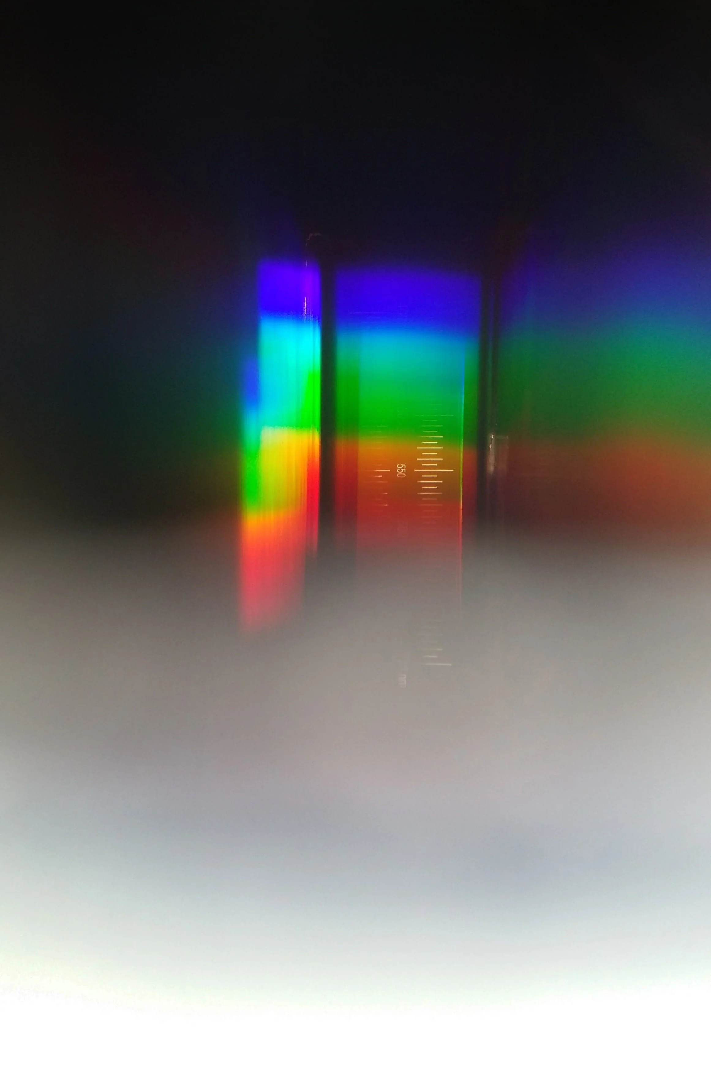 Close-up of a clear glass prism dispersing light into a rainbow spectrum with visible measurement markings.