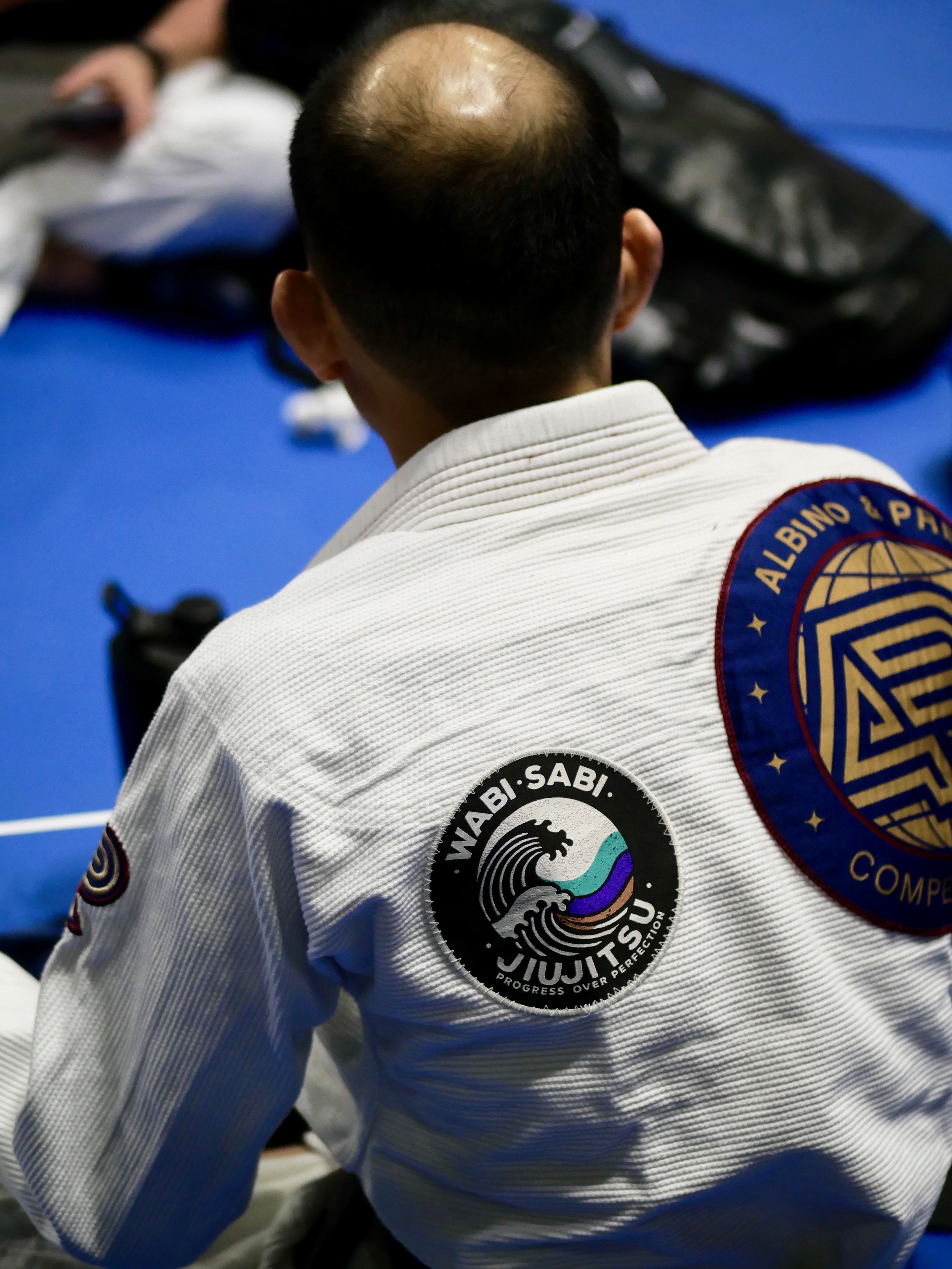 Person in a jiu-jitsu gi with Wabi-Sabi Jiu Jitsu logo patch, sitting on a mat.