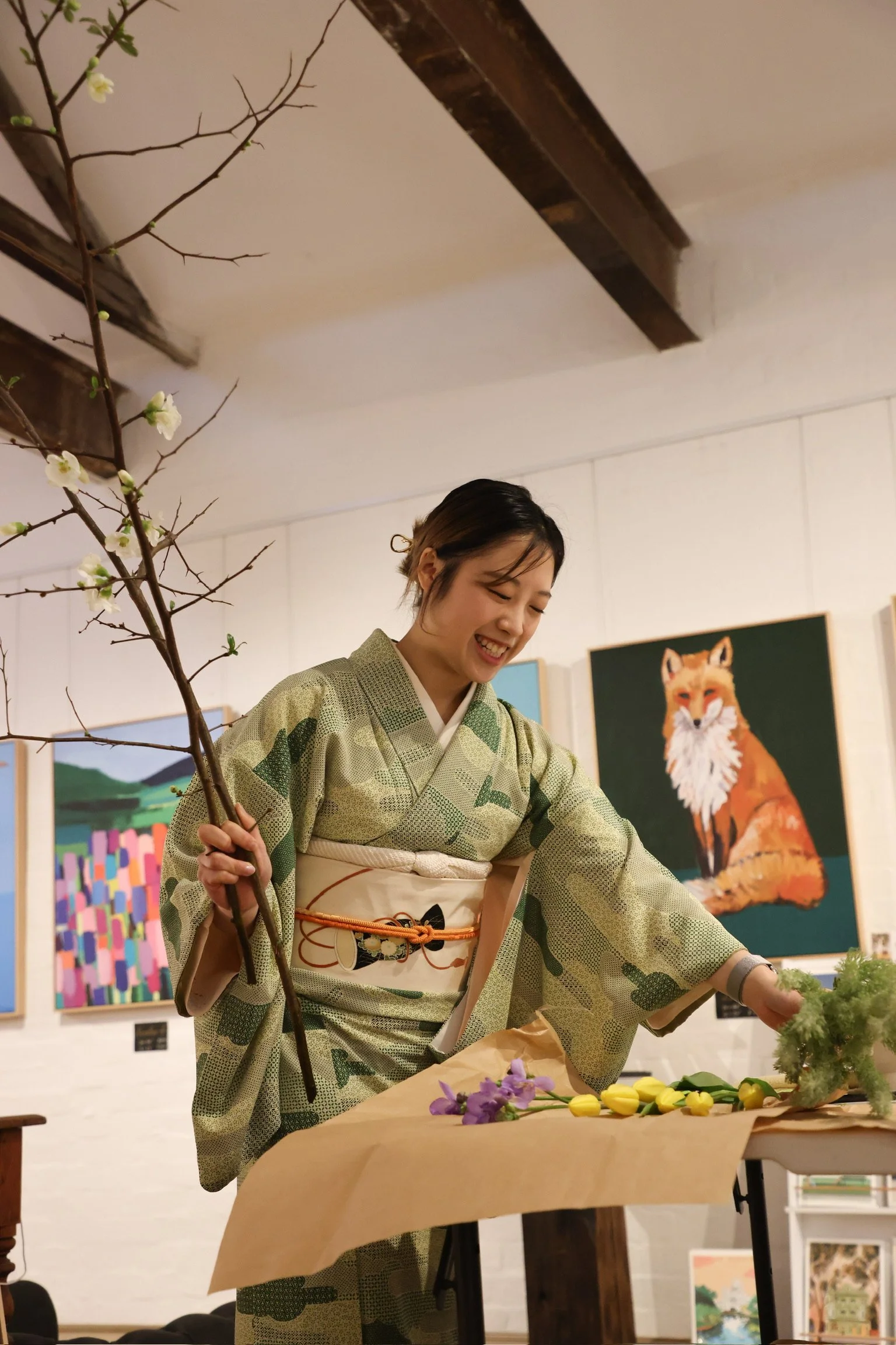 Person arranging flowers while wearing a green kimono in an art gallery.