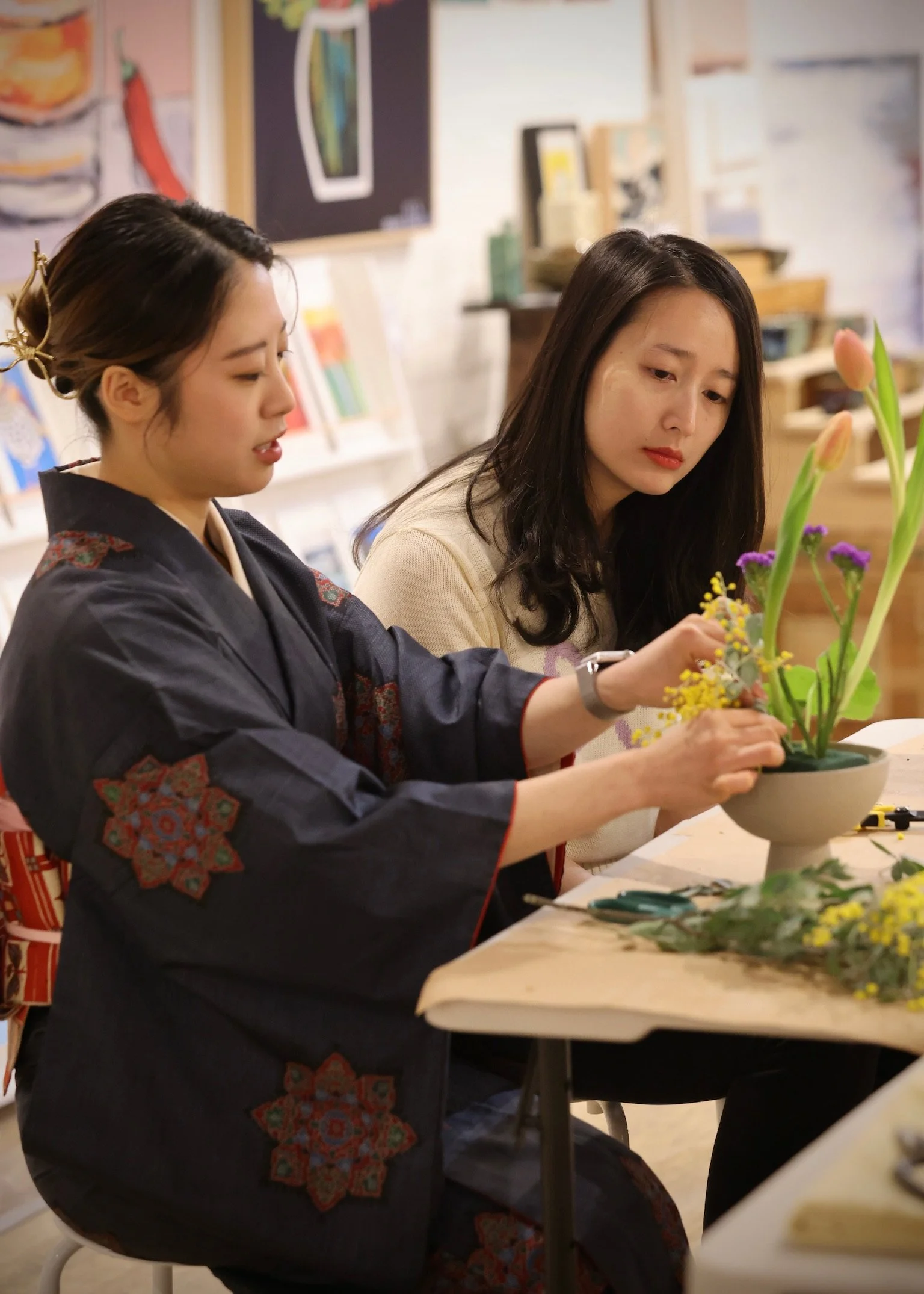 Two women at a table arranging flowers in a pottery class.