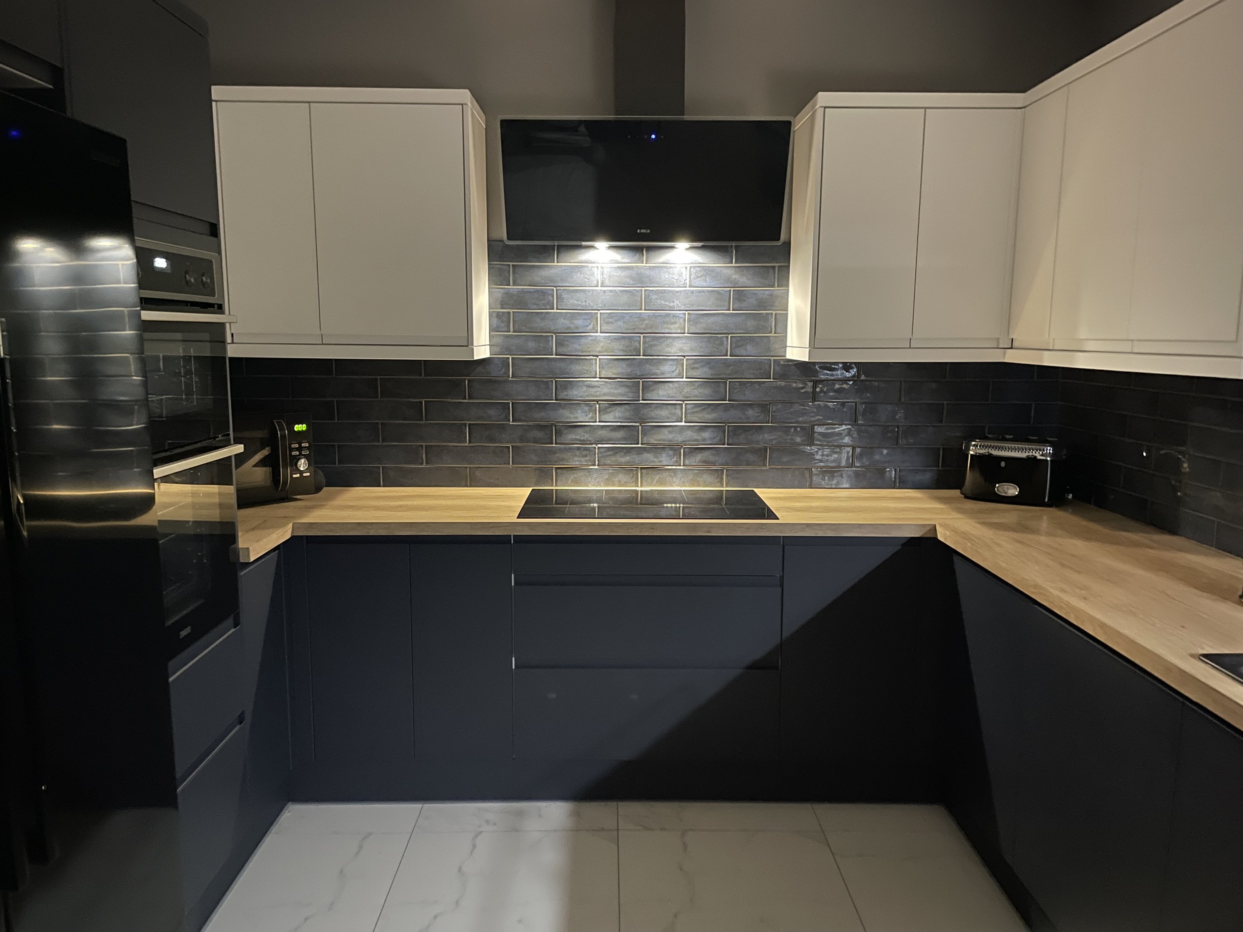 Front view of blue and white kitchen with mood lighting, black appliances and white tiled floor