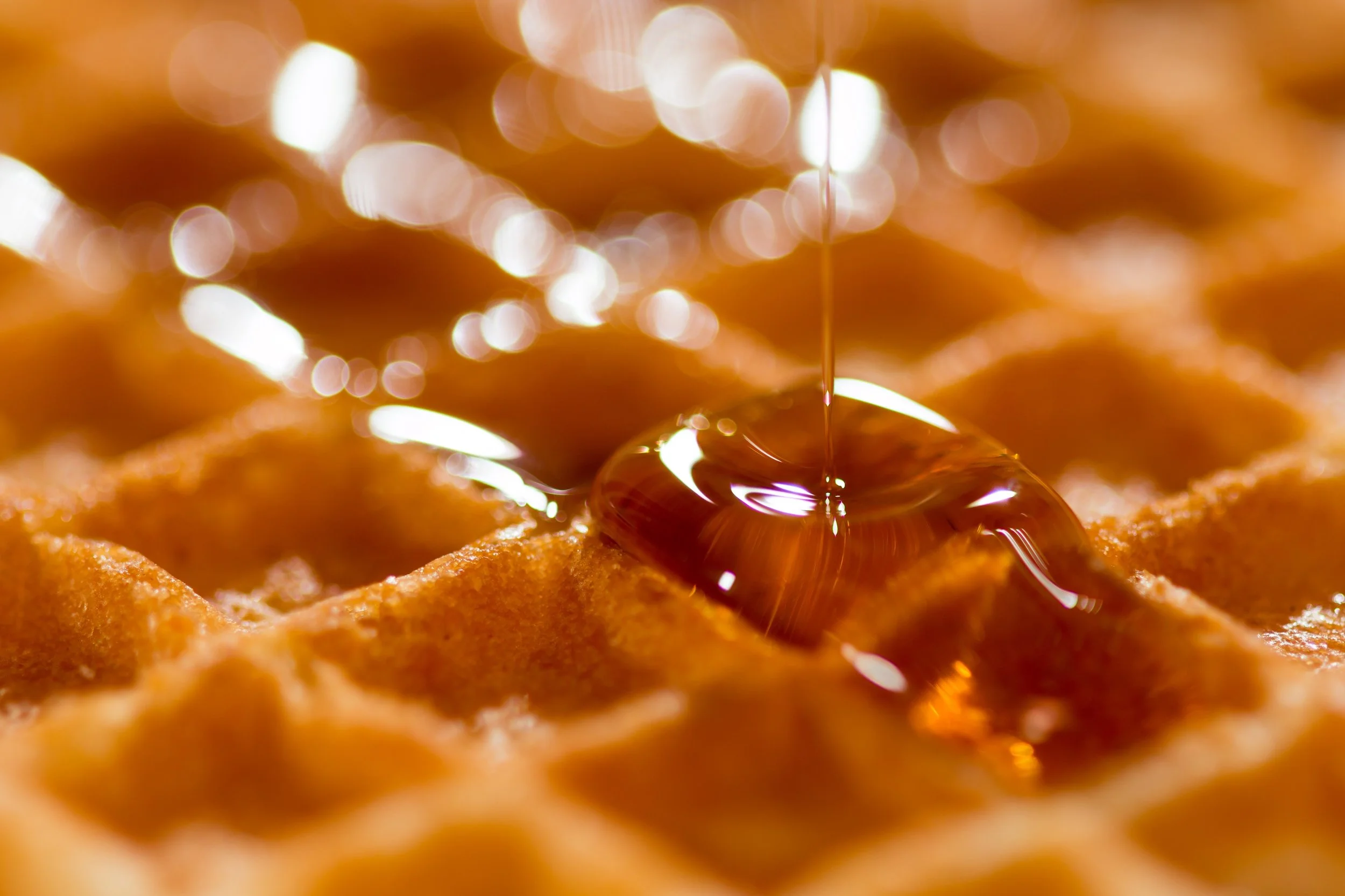 Close-up of honey being drizzled onto a waffle, with a golden, bubbly, and syrupy appearance.