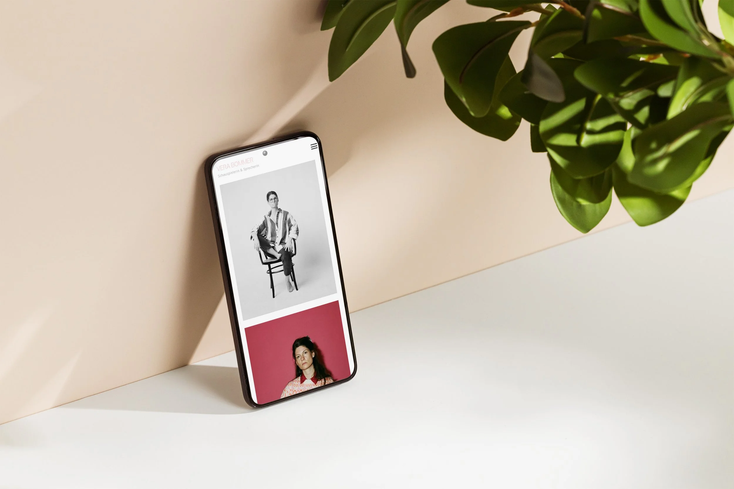 Smartphone auf weißem Tisch, zeigt Fotos, links eine schwarze und weiße Aufnahme, rechts eine farbige Aufnahme. Grüner Pflanzenzweig im oberen rechten Bildbereich.