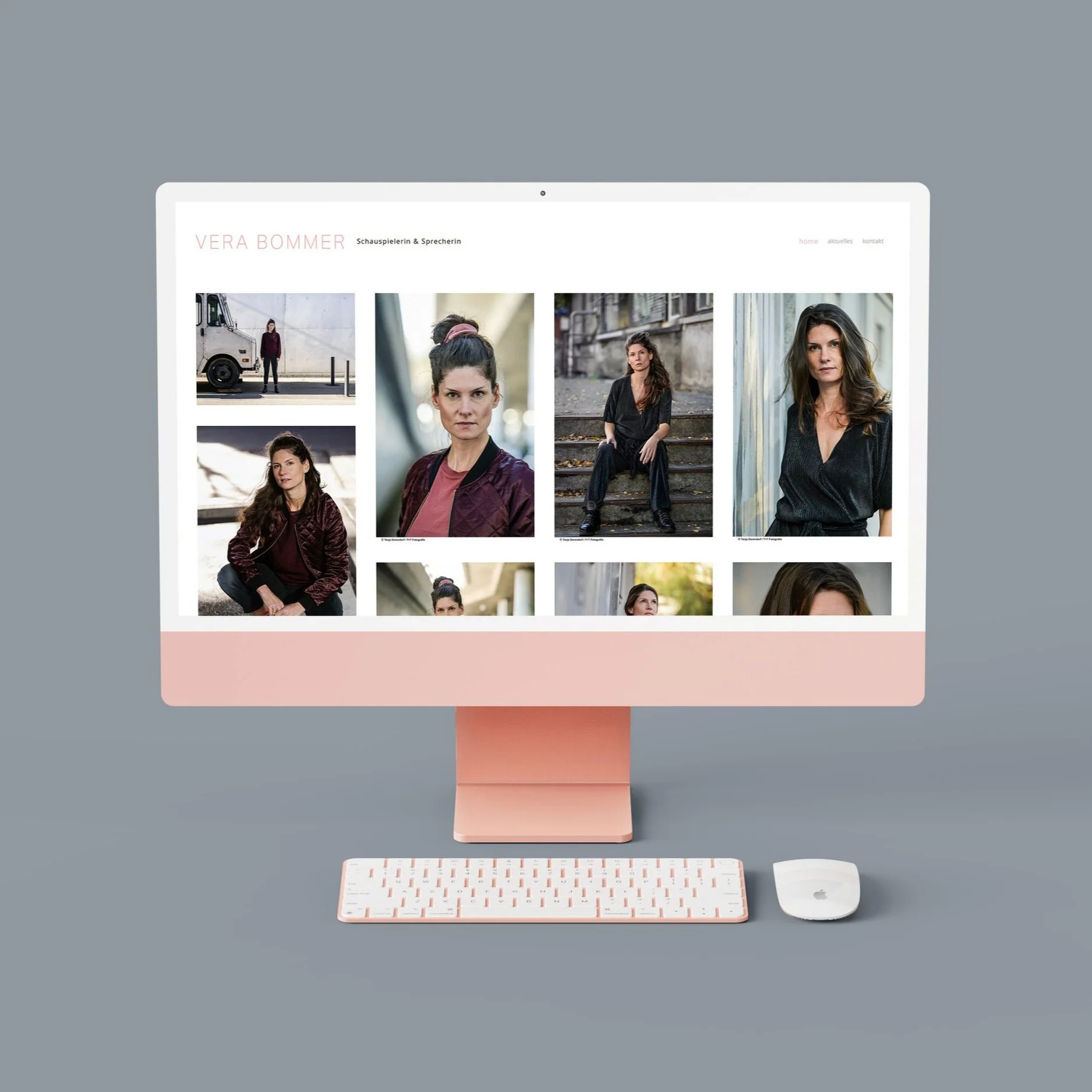 Ein Apple iMac-Computer mit rosa Gehäuse, einer weißen Tastatur und einer weißen Maus auf einem grauen Tisch. Der Bildschirm zeigt eine Webseite mit Fotos einer Frau und Text in Deutsch.